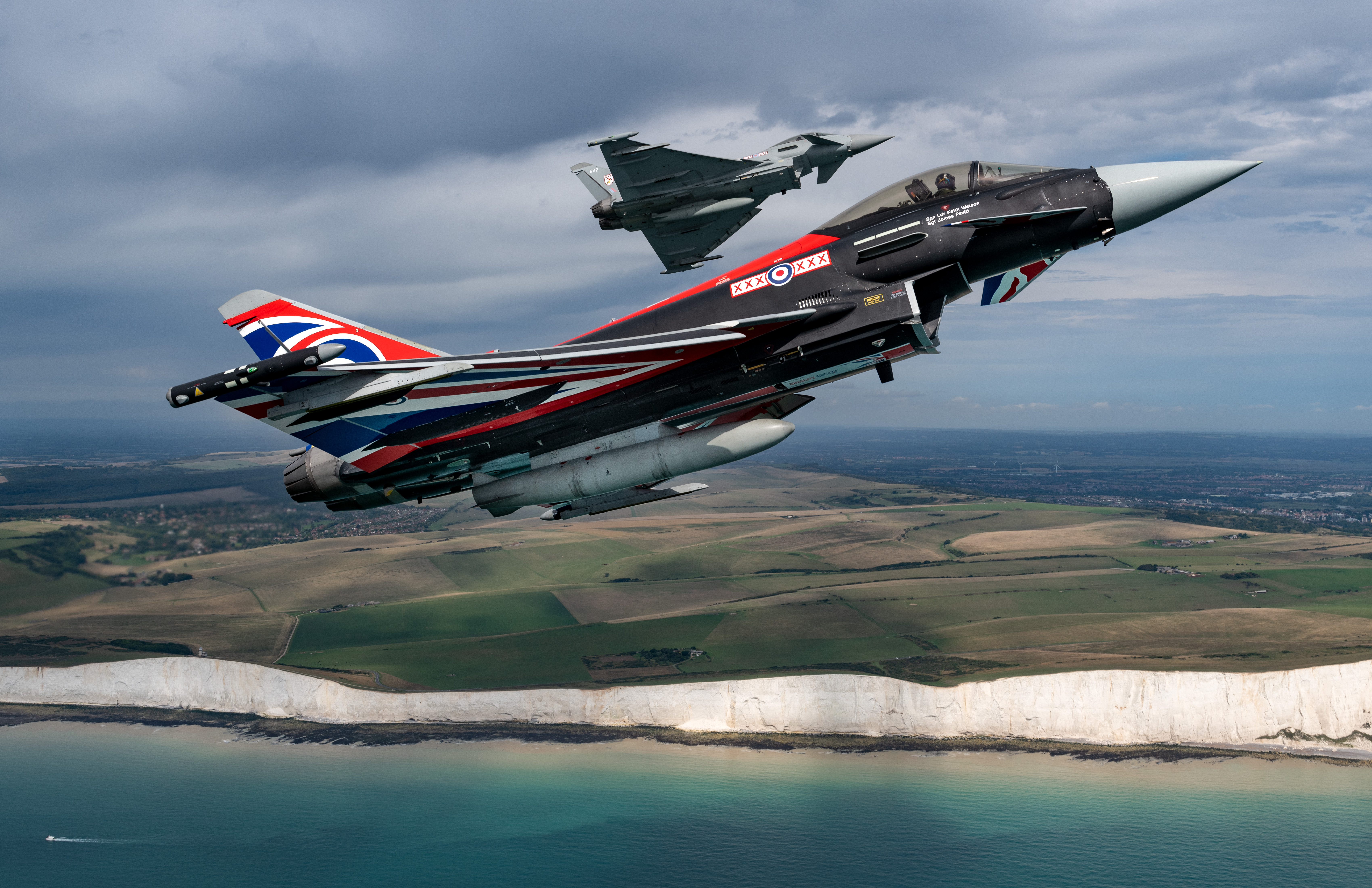 Image shows two Typhoons with Union Jack paint in flight over the white cliffs.
