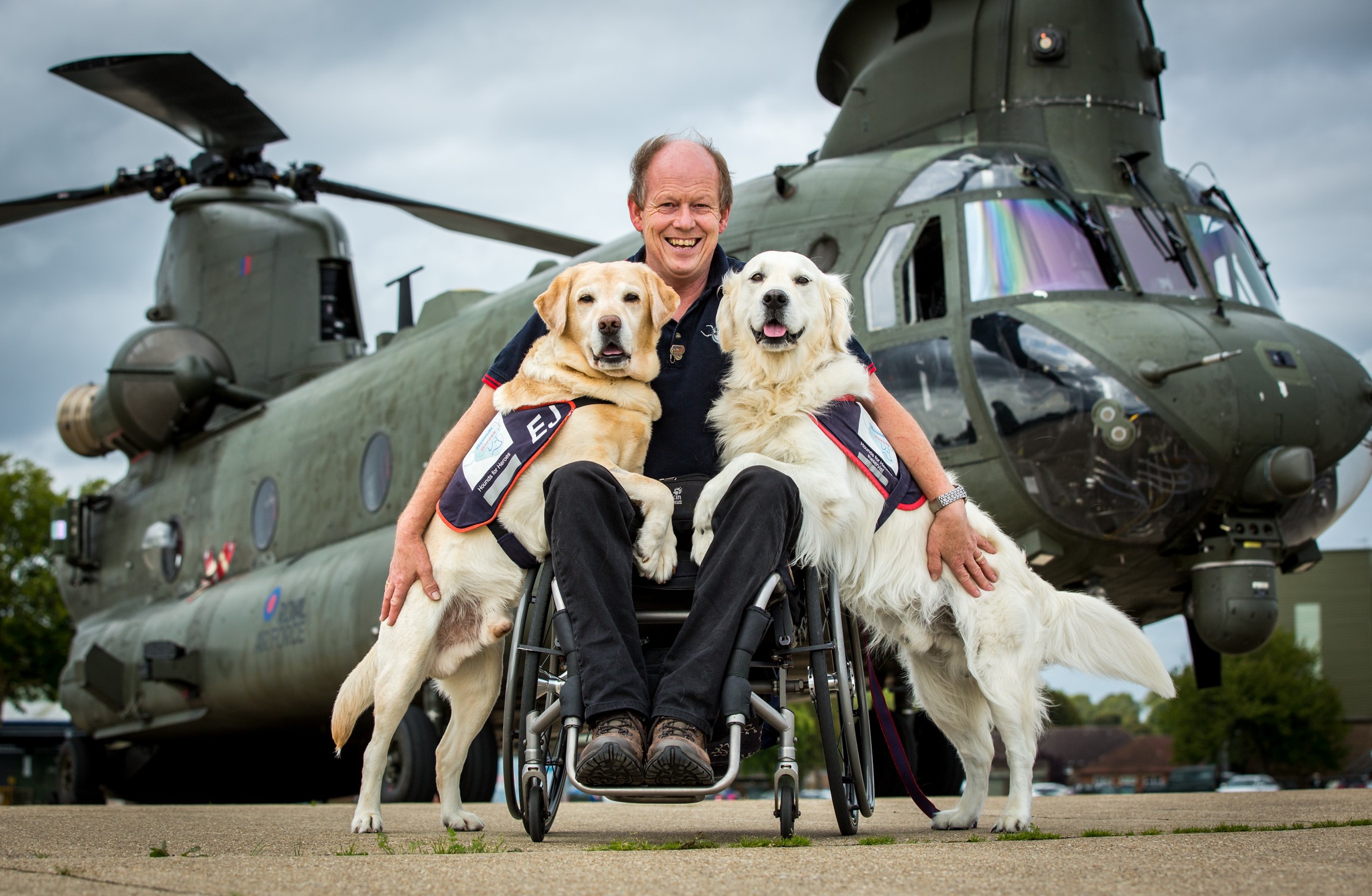 Image shows veteran with two Assistant Dogs in front of a Chinook helicopter. 