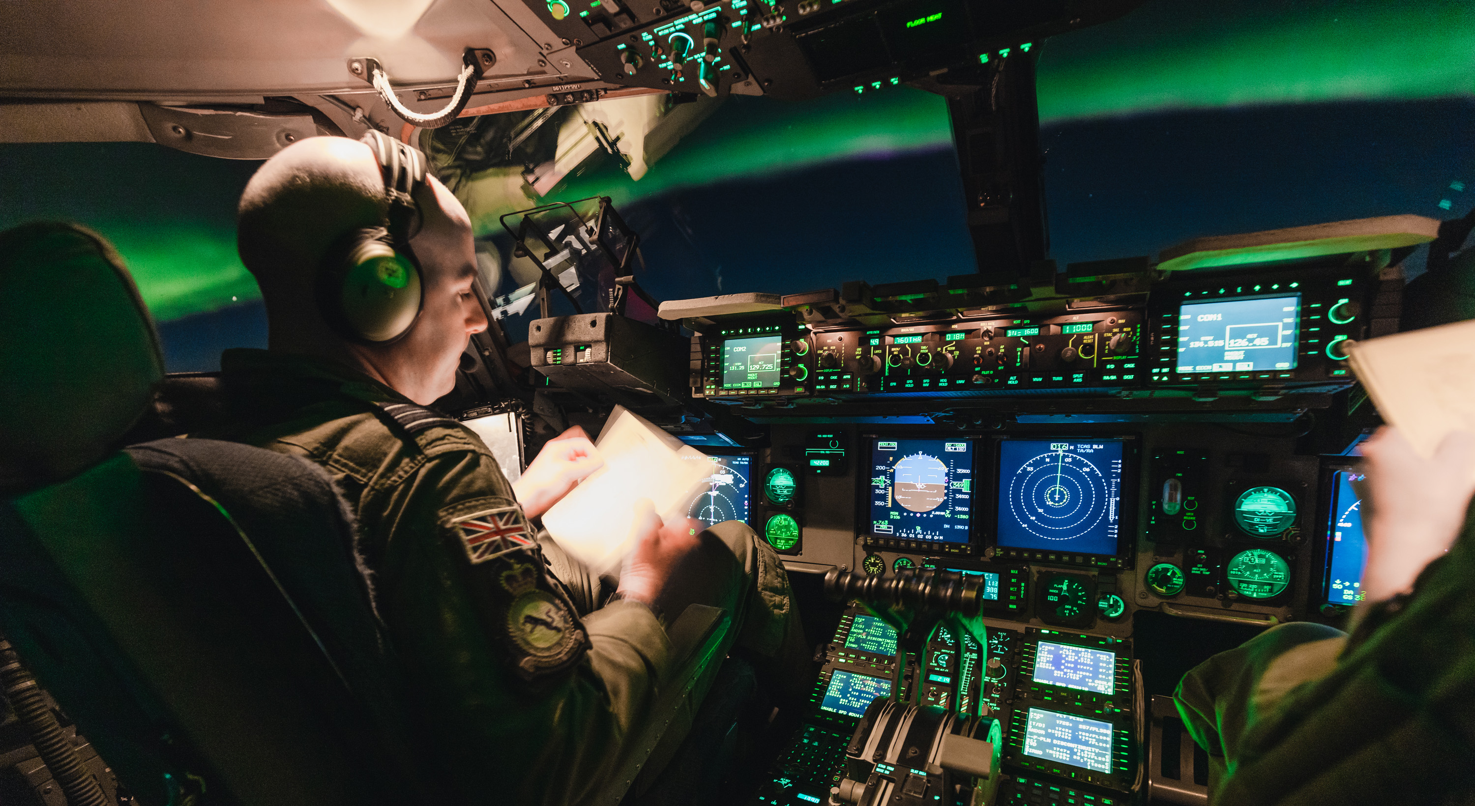 Image shows RAF Pilots in the cockpit of the Globemaster aircraft, looking towards the Northern Lights.