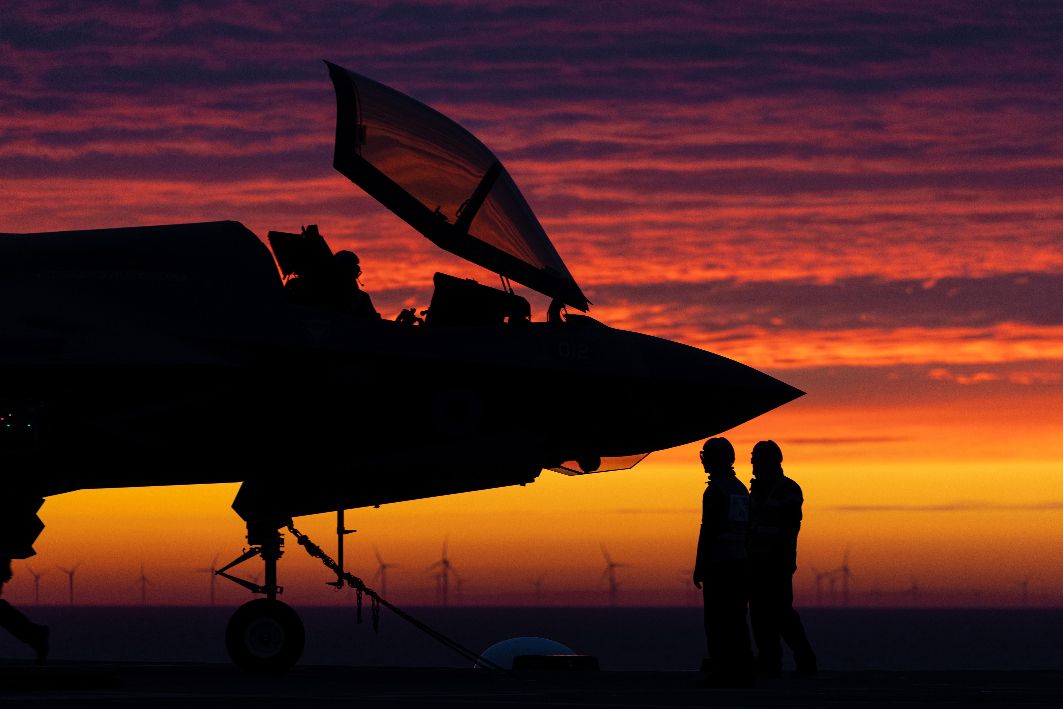 Image shows the open cockpit of a RAF Typhoon and pilots on the airfield during a sunset.