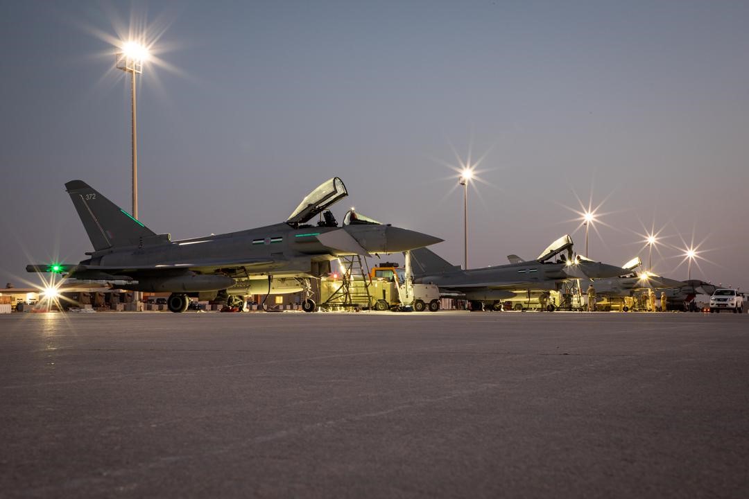 Typhoons on the runway at dusk, with airfield lights on. 
