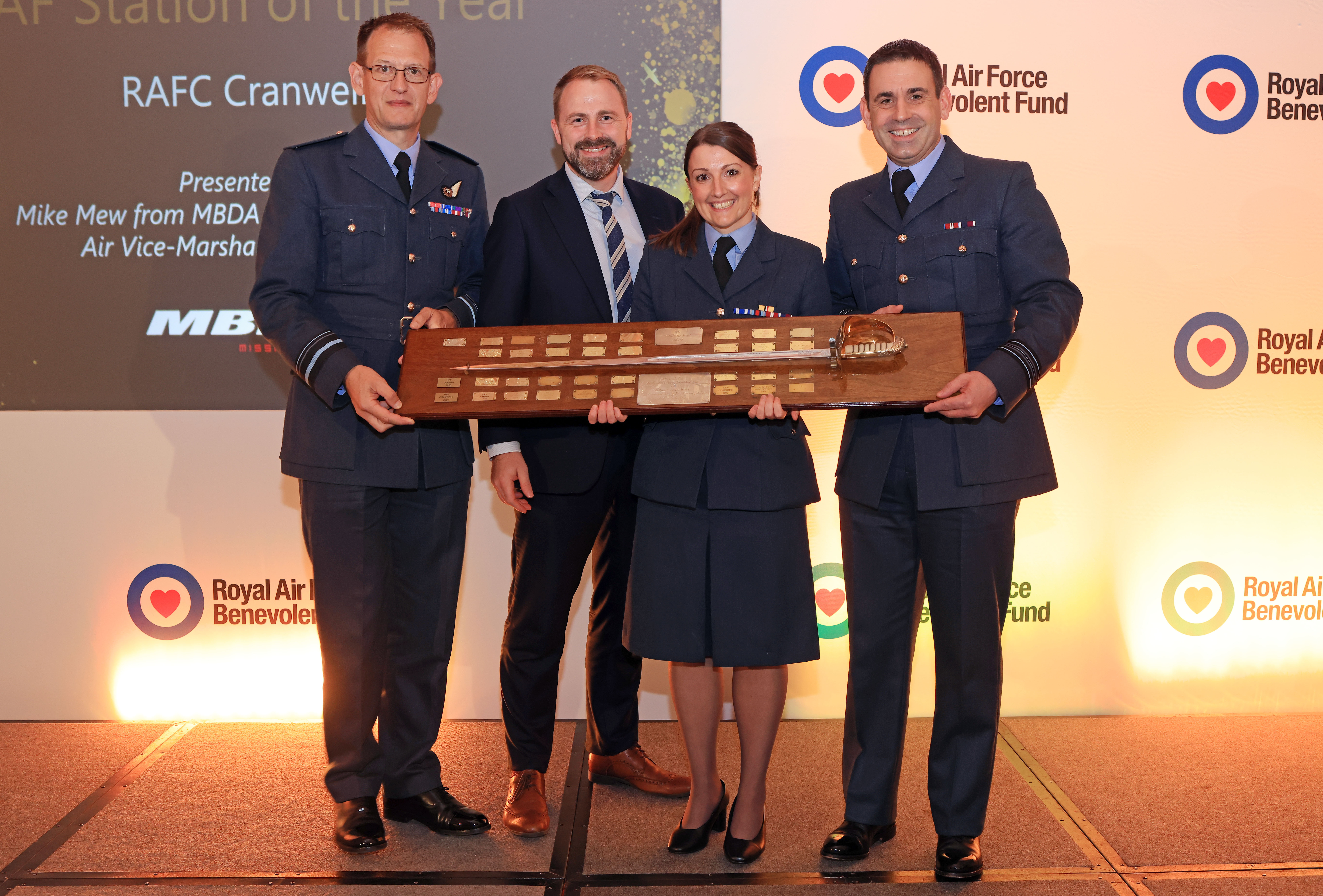 Personnel hold their award; a sword on a plaque.