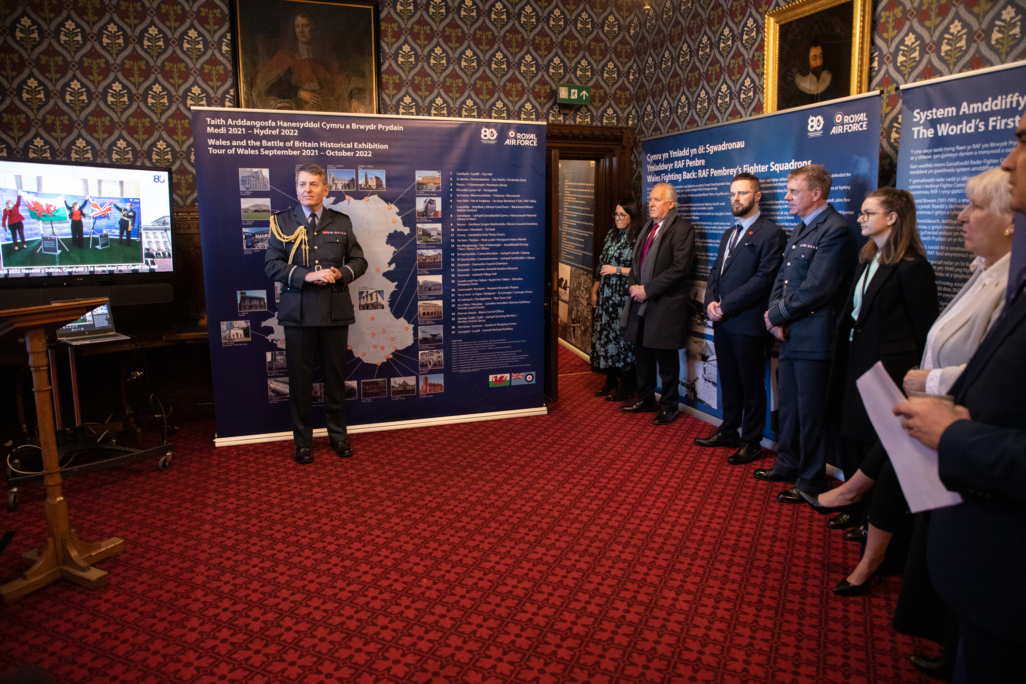 Image shows RAF aviator and civilians watching presentation at exhibition.