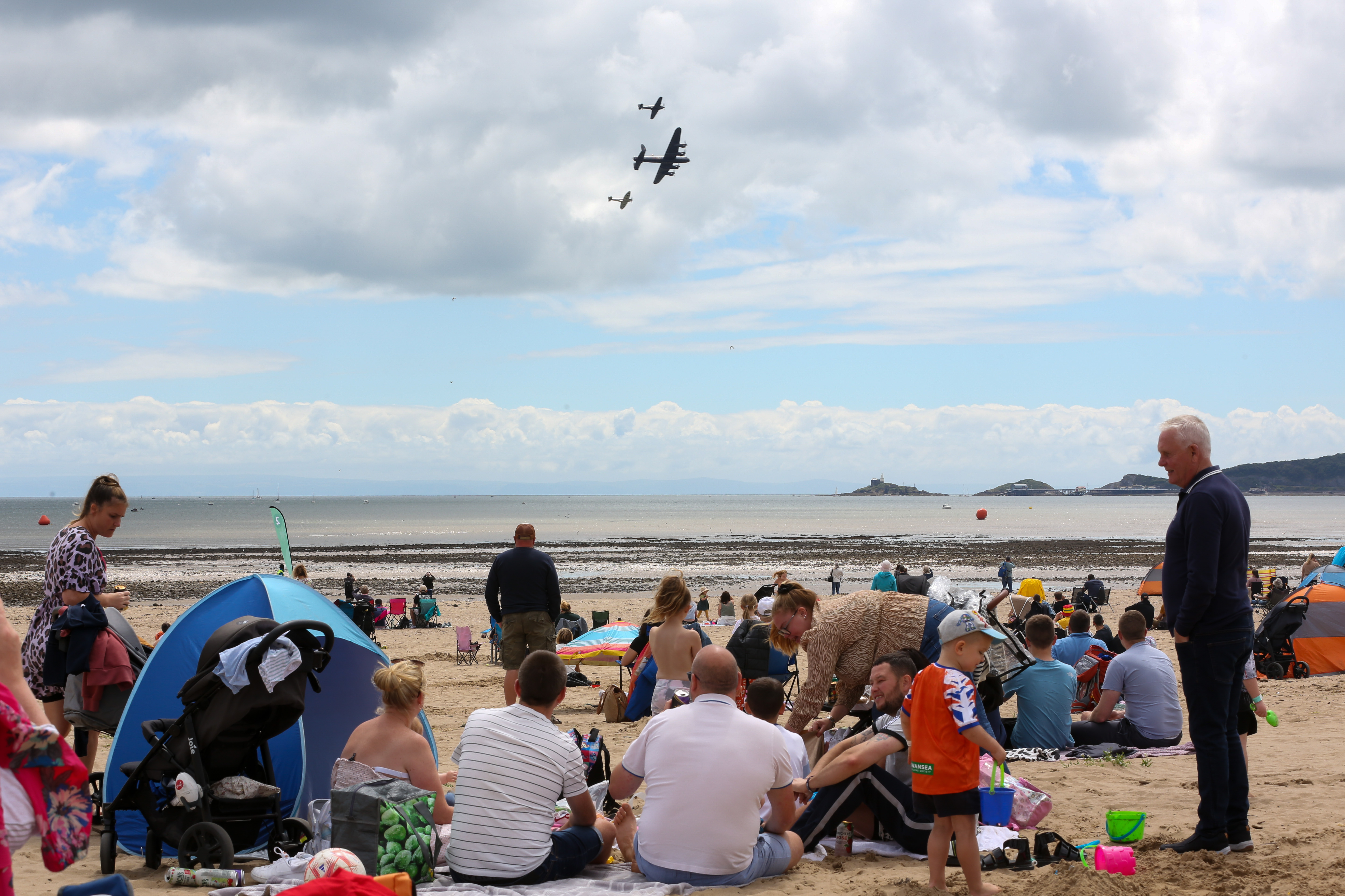 Image shows a Lancaster and two Spitfires flypast over the public beach.