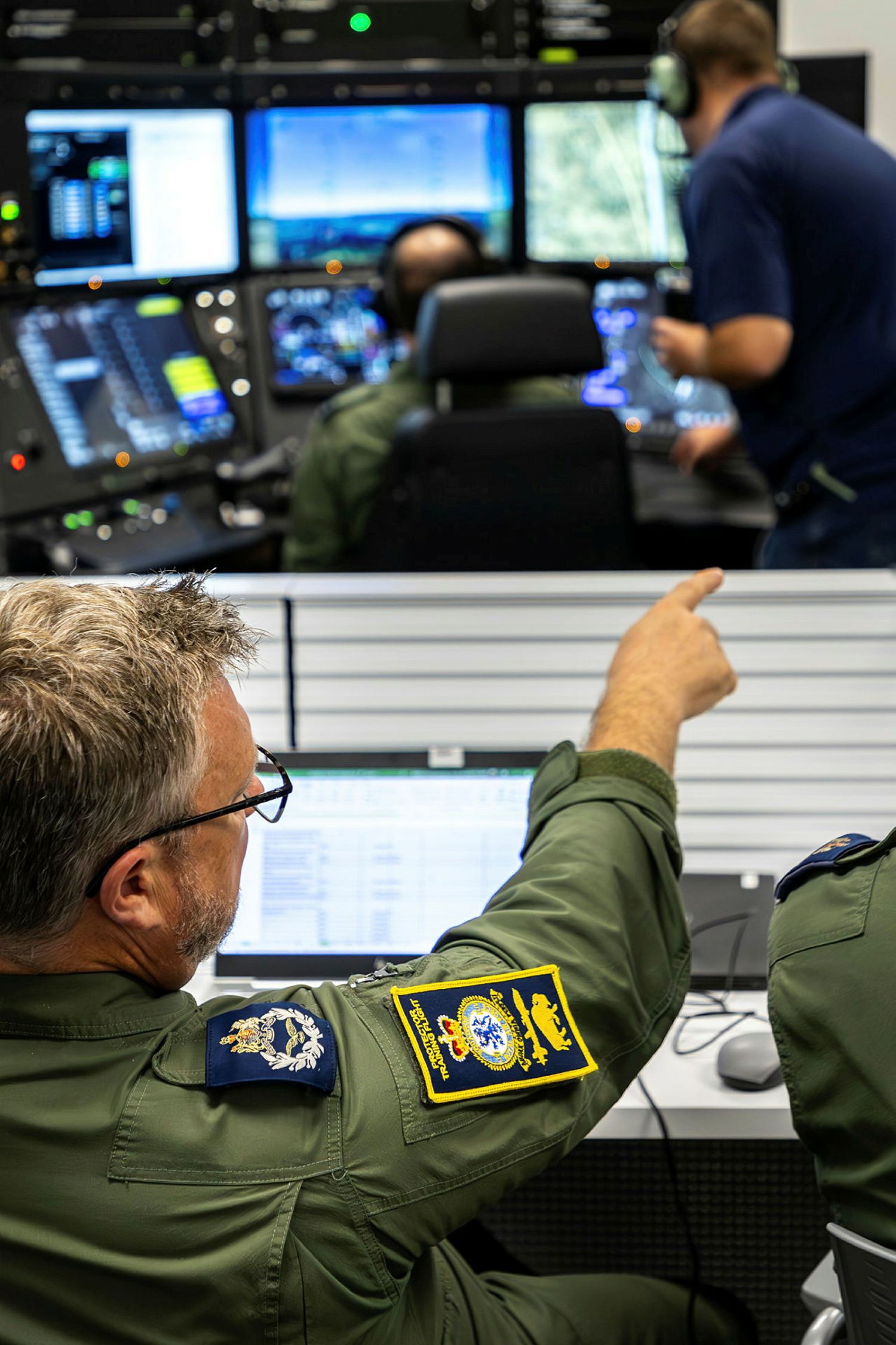 RAF personnel in training room, personnel pointing in the foreground and screens in the background.