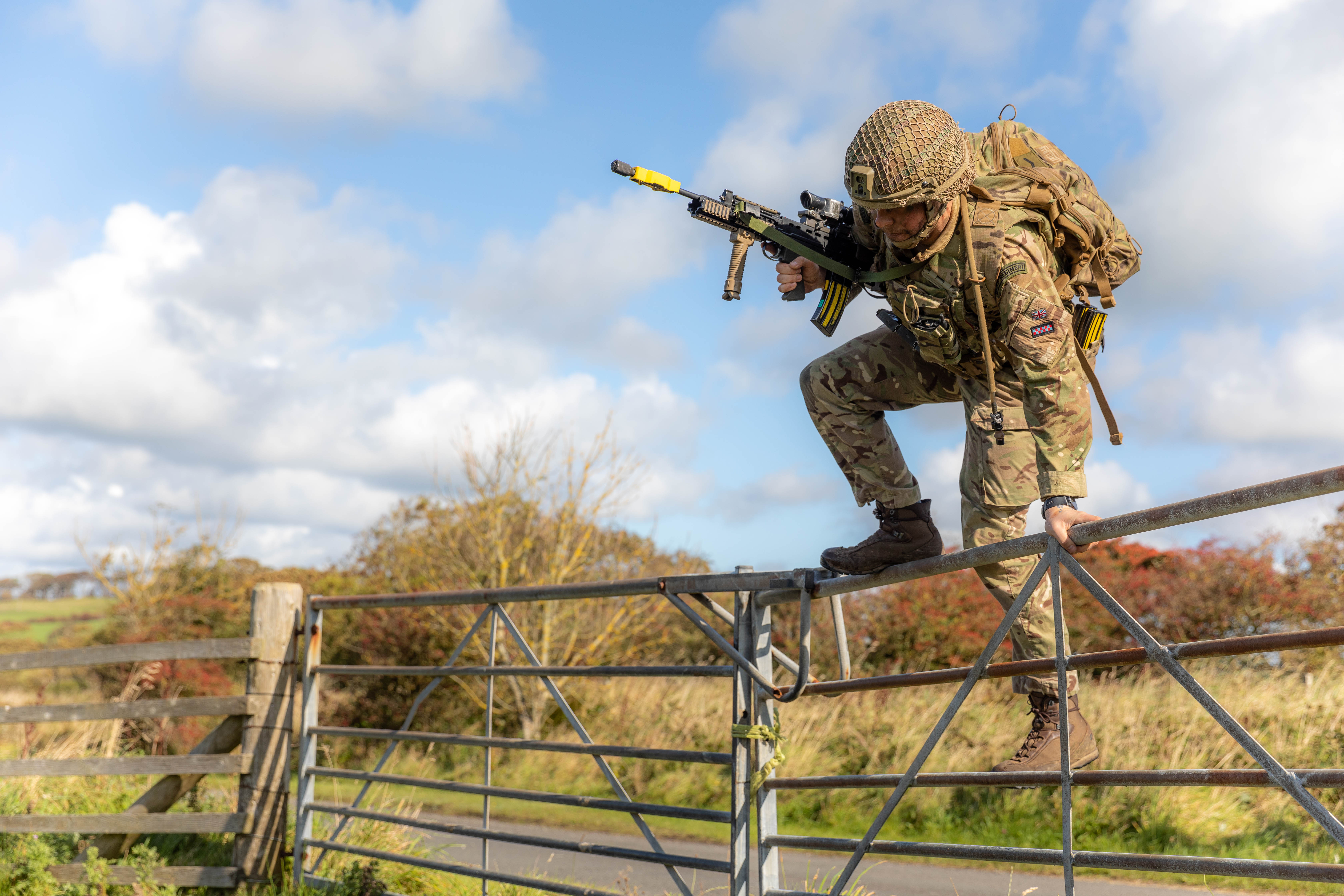Soldier jumping over a farm gate, carrying a rifle