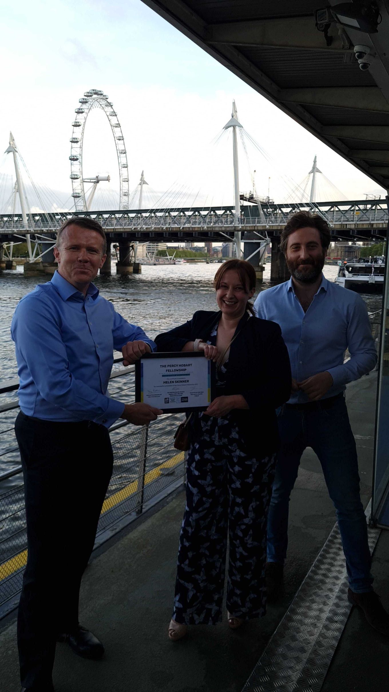 Three people on the course holding a framed certificate, in-front of the London Eye and Thames.