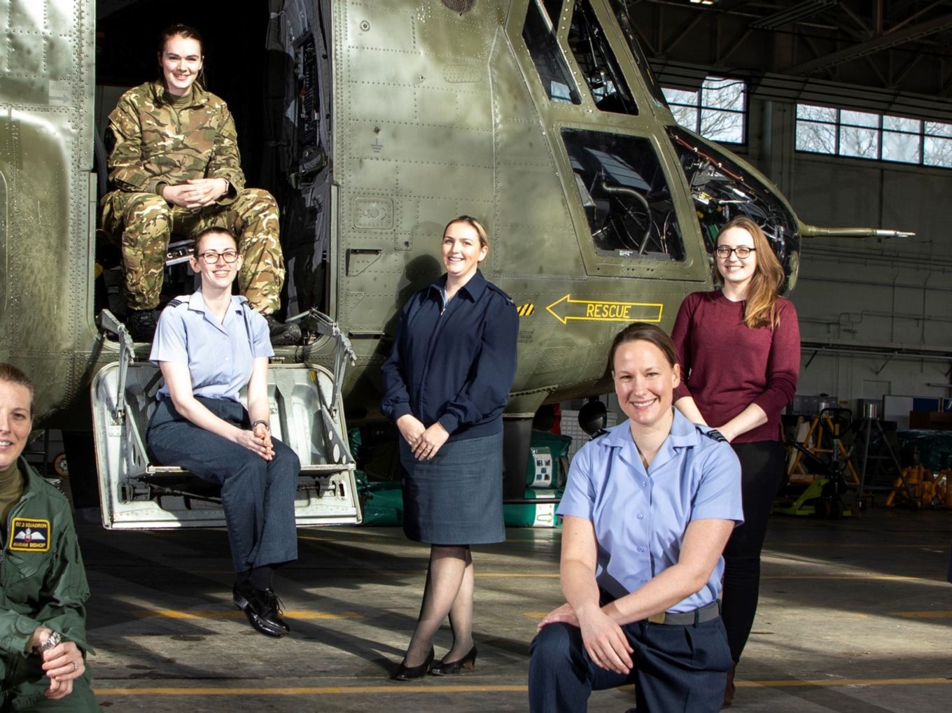 Women personnel smile by the front of a Chinook helicopter.
