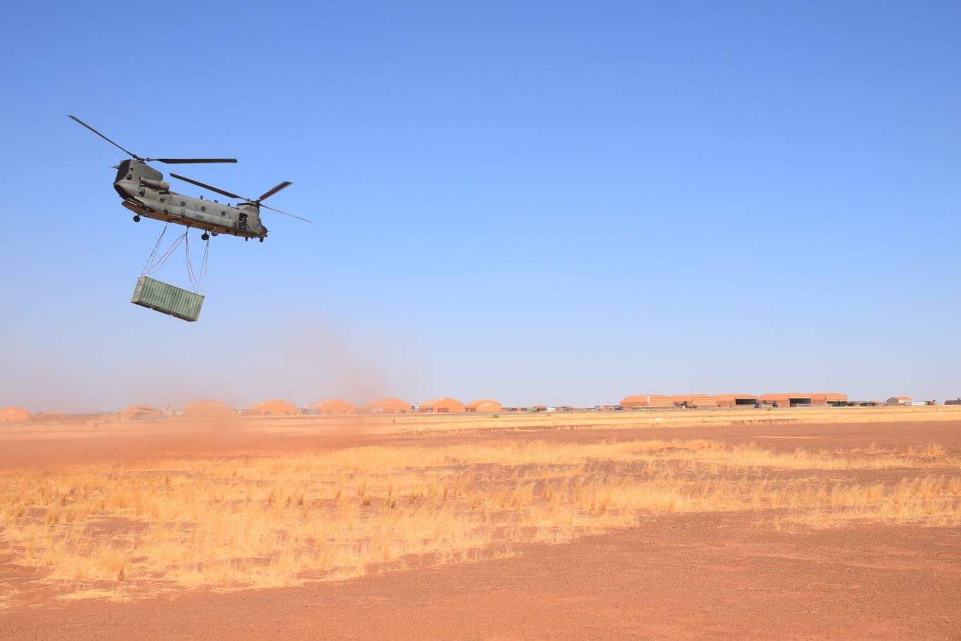 Image shows RAF Chinook in the desert with the container hanging below.