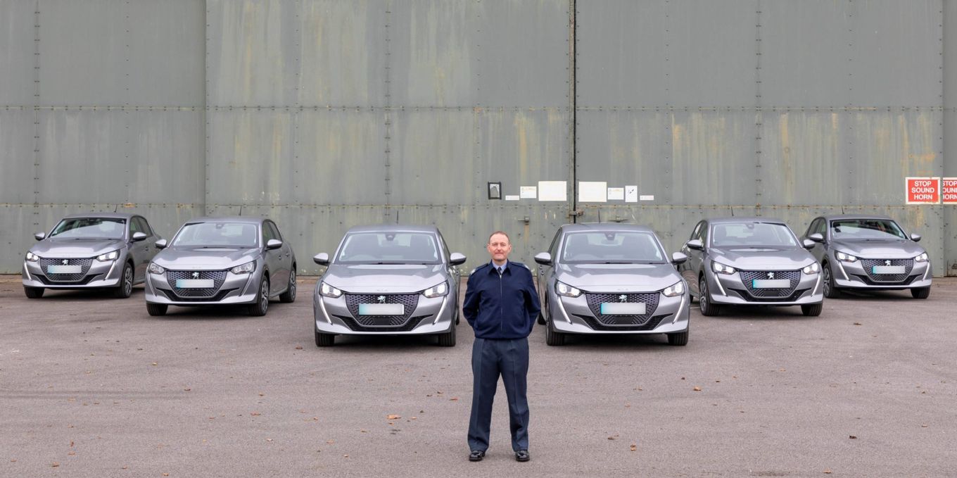 Image shows an RAF Warrant Officer standing in front of the six new Peugeot e-208 electric vehicles at RAF Leeming.