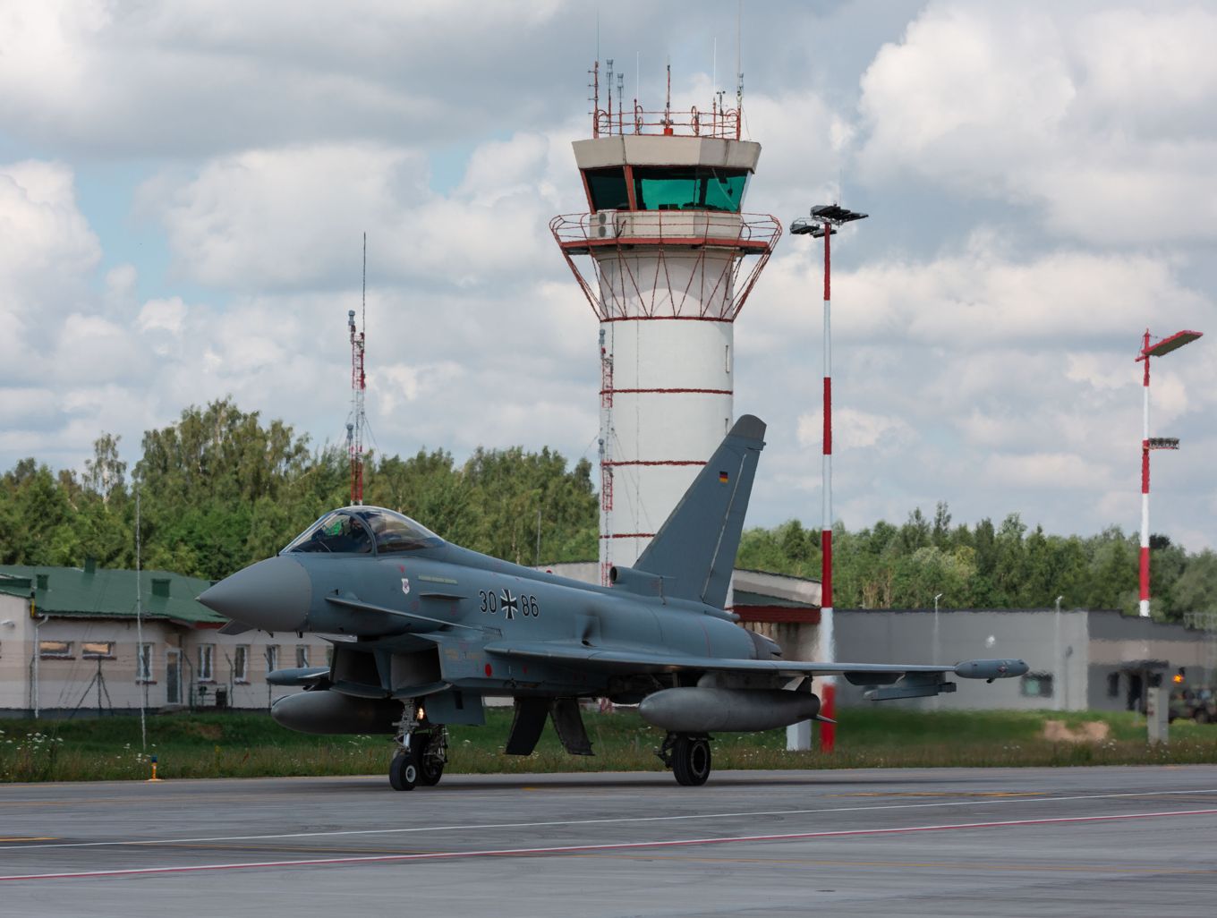 Image shows German Air Force Eurofighter taxiing on arrival with air traffic control tower in the background.