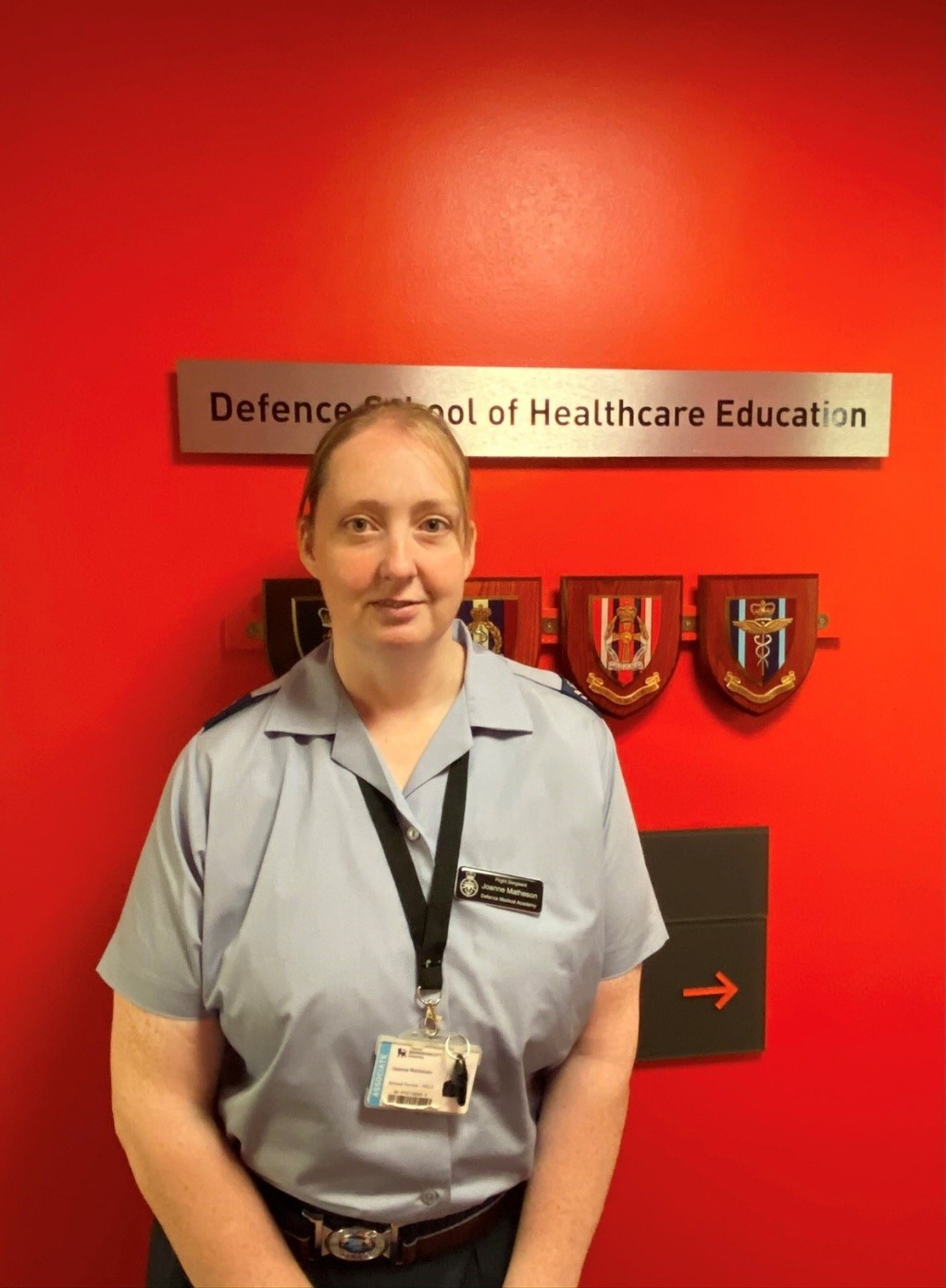 Flight Sergeant Matheson standing in-front of a red wall displaying Defence School of Healthcare Education crests. 