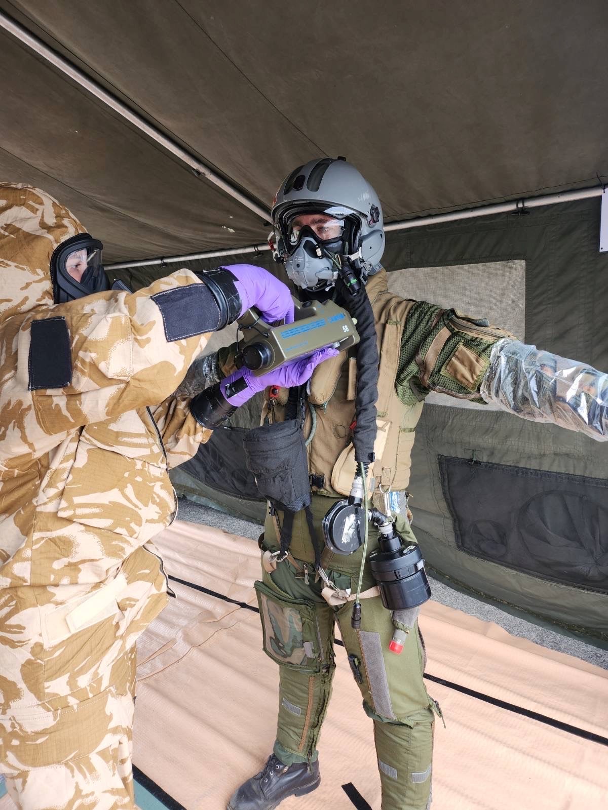 Personnel in full CBRN protective kit, scanning a pilot for CBRN particulates