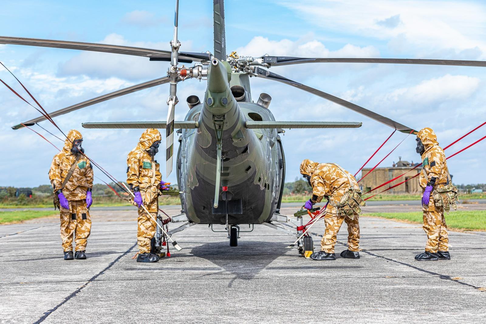 Personnel dressed in CBRN protective kit, clean down a helicopter