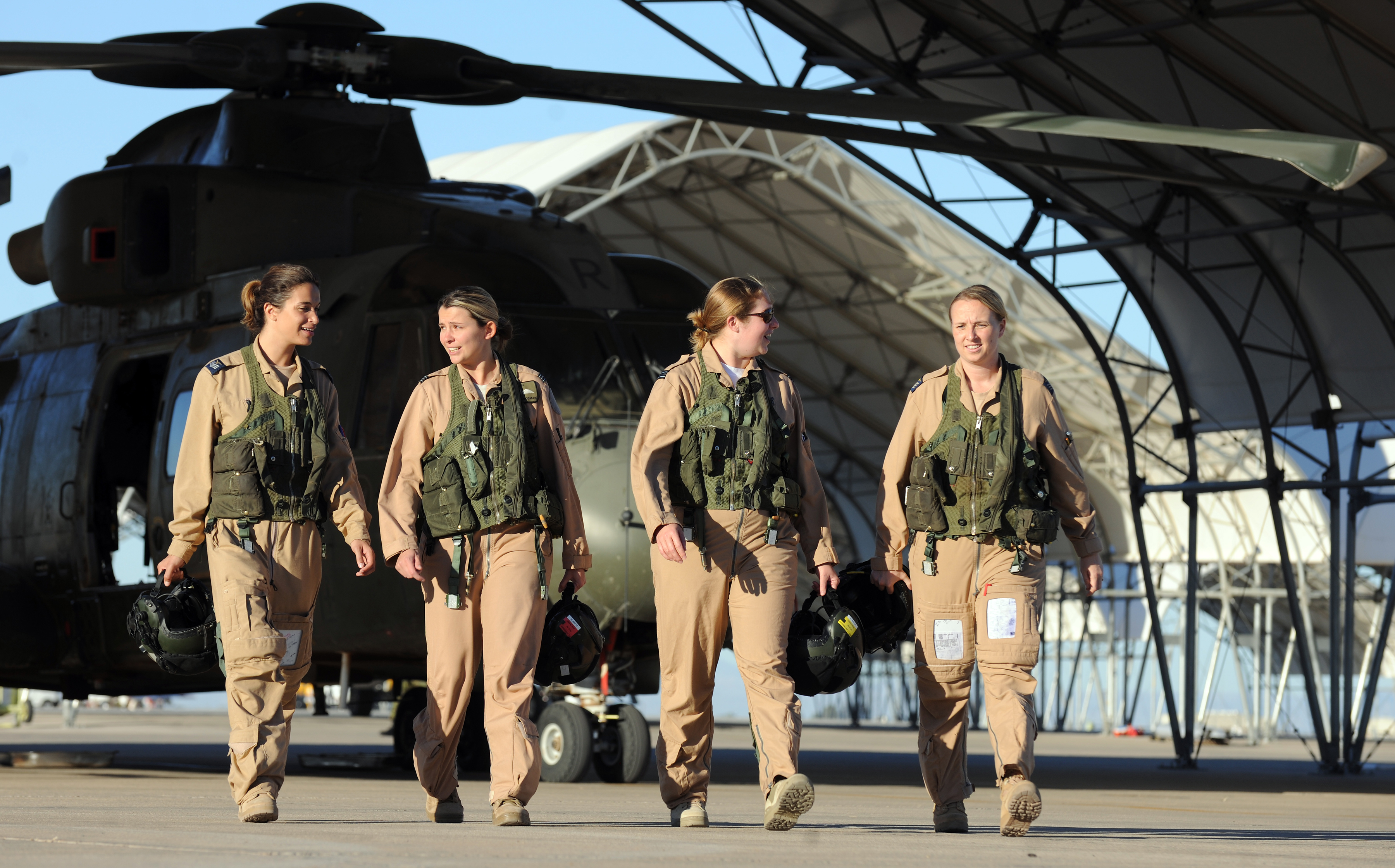Image shows RAF Aviators walking by hangar and helicopter.