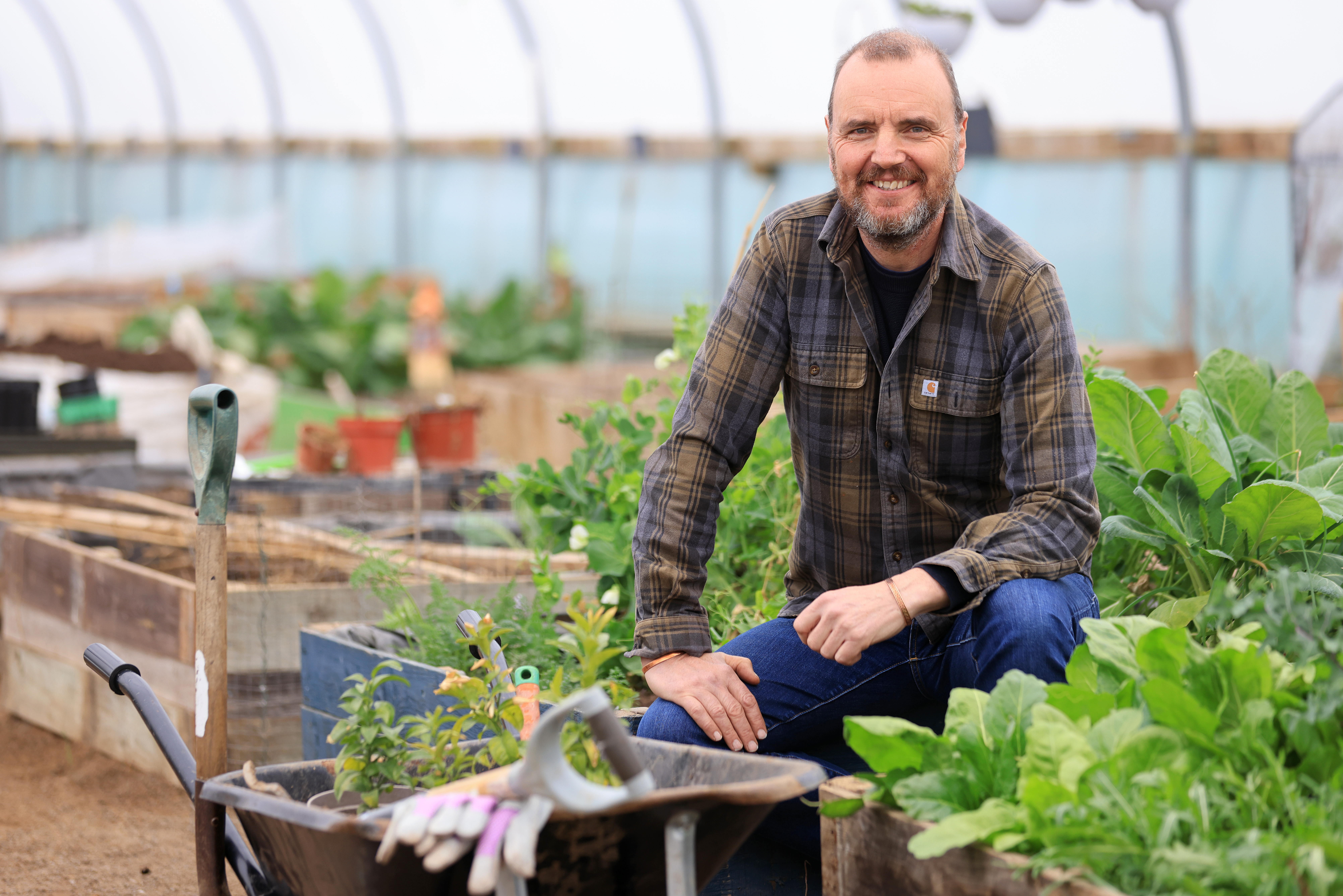 John sits among plant boxes and gardening equipment.