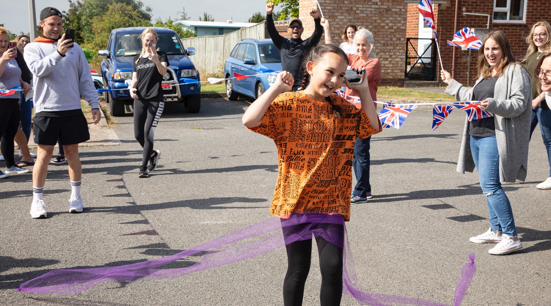 Ryan cheers Katie over the finish line as Chris and Katie's Mum film the occasion. They're surrounded by friends, family and teaching staff as they cheer her over the line.