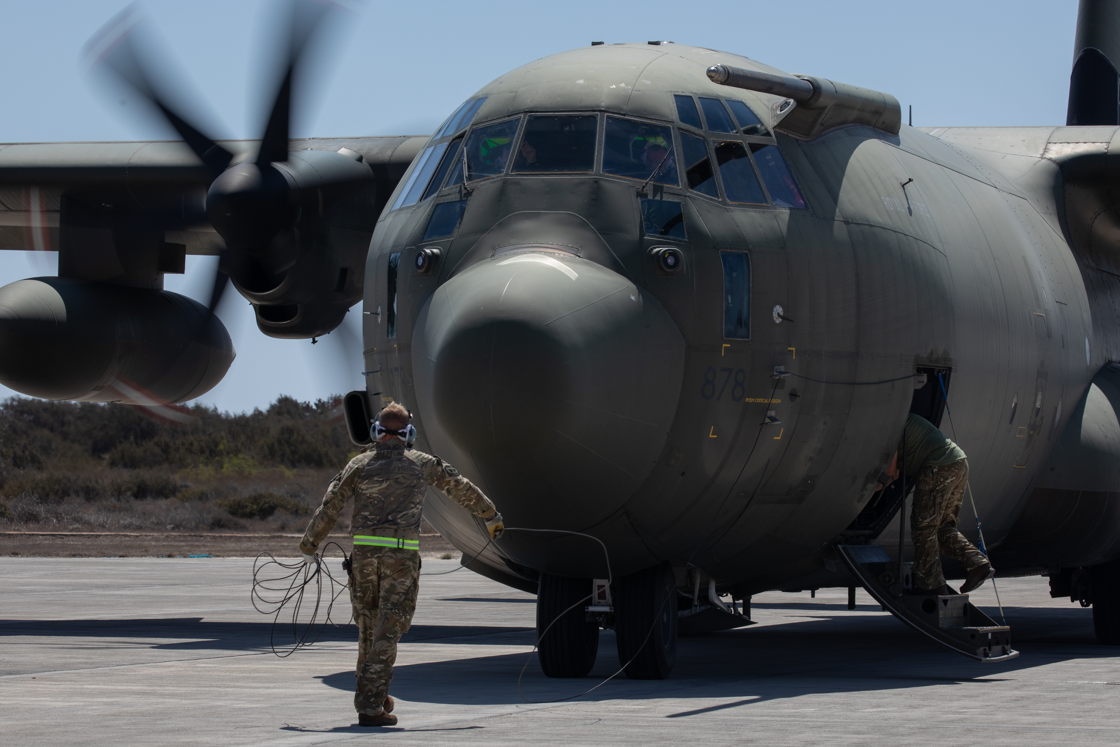 Image shows RAF Hercules on the airfield with aviator guiding it. 