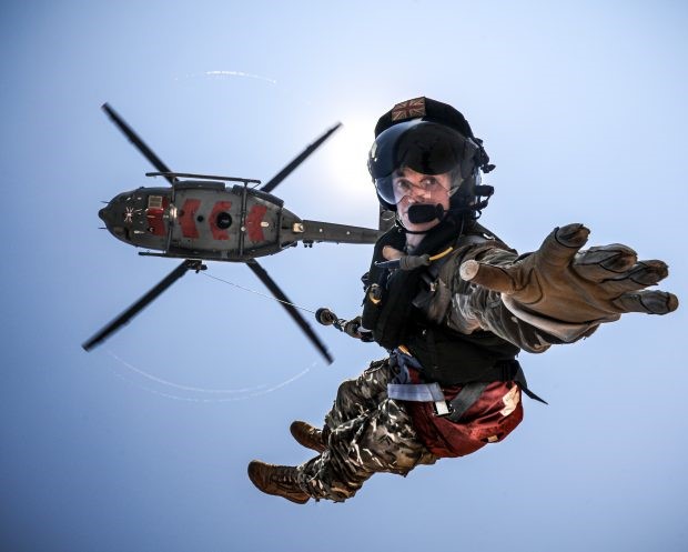 Personnel leans out towards the camera as he zips from helicopter.