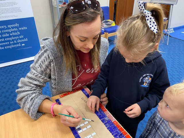 Image shows school children and civilian working on mosaic at a table.