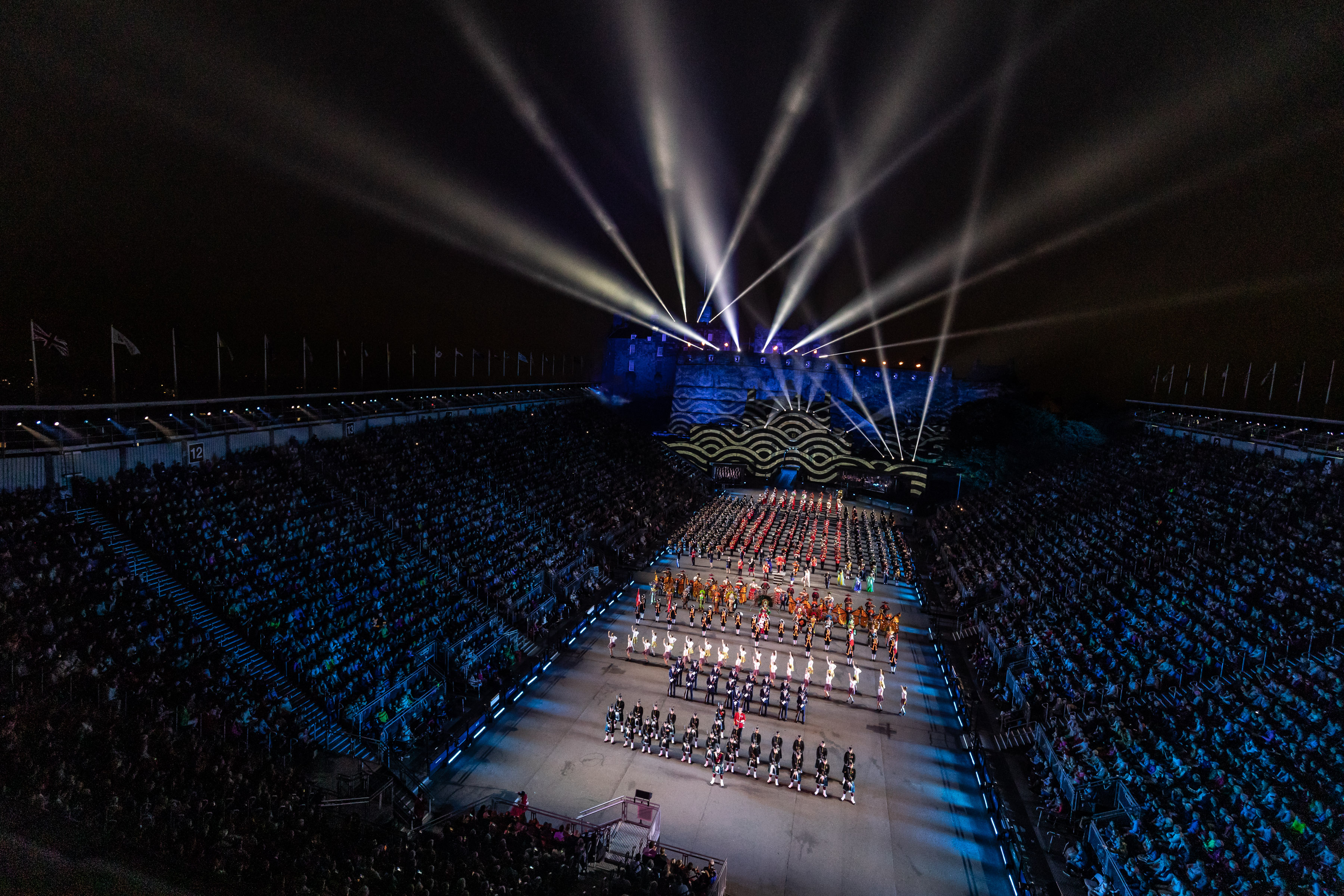 Image shows parade with crowds watching and spotlights emitting from Edinburgh Castle