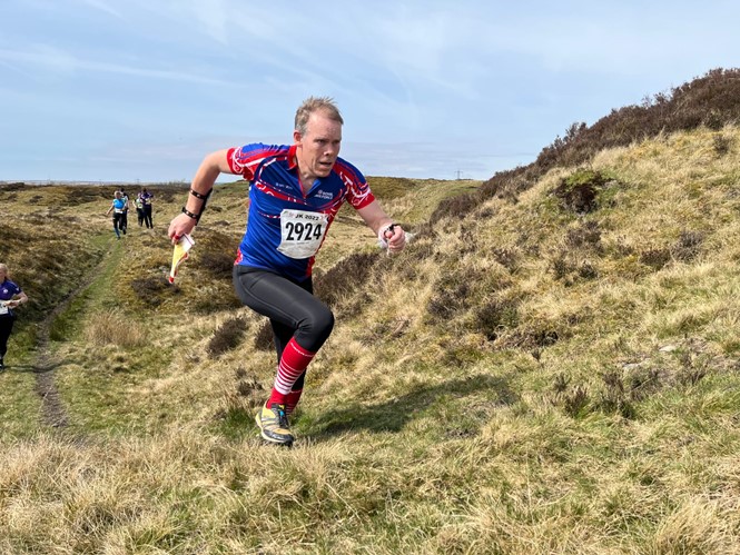 Orienteer runs uphill on the moorland.