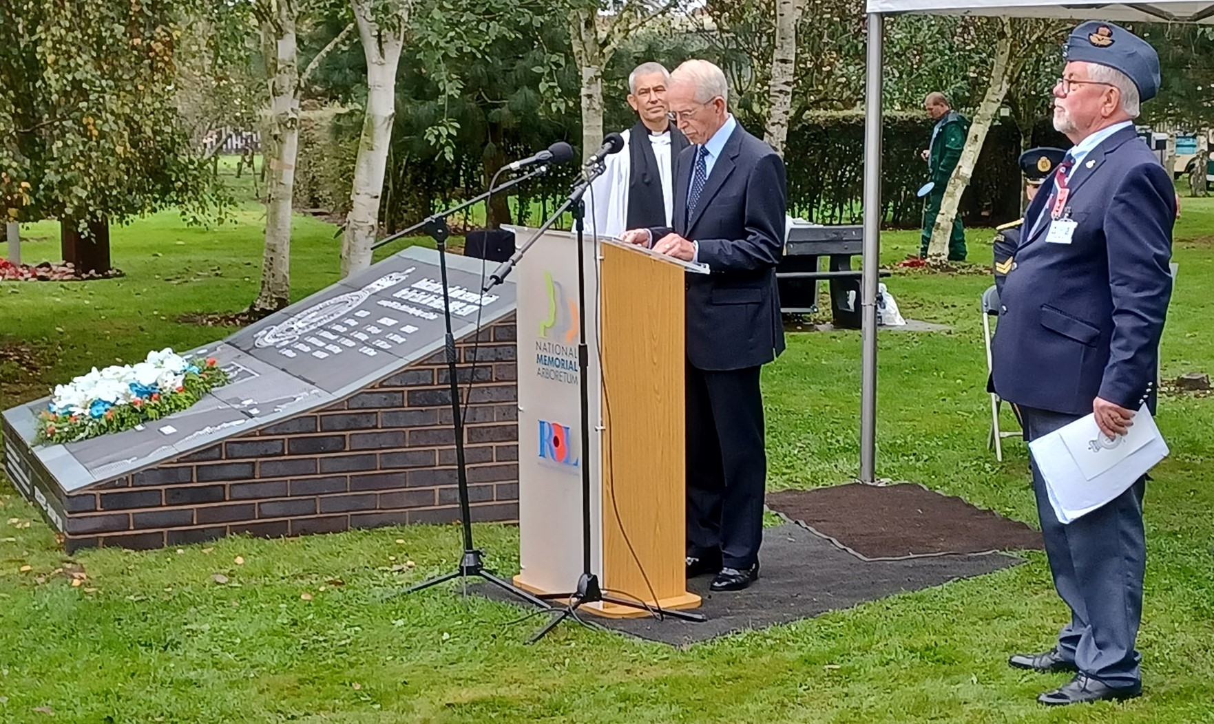Personnel reading at oration stand at ceremony with Memorial.