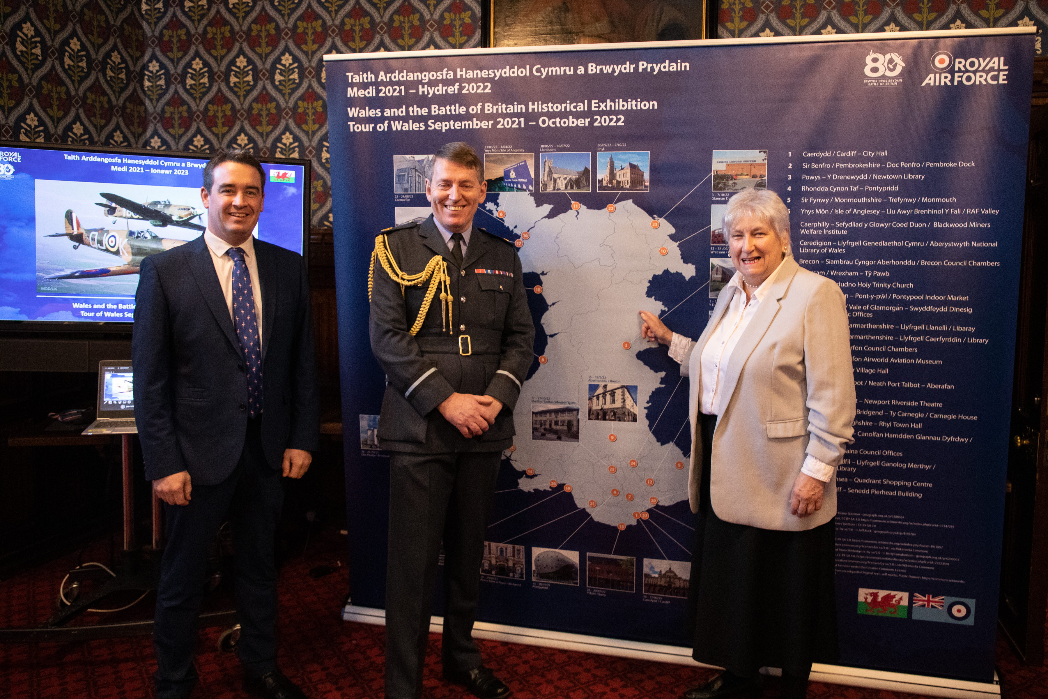 Image shows RAF aviator and civilians standing by information board at exhibition.