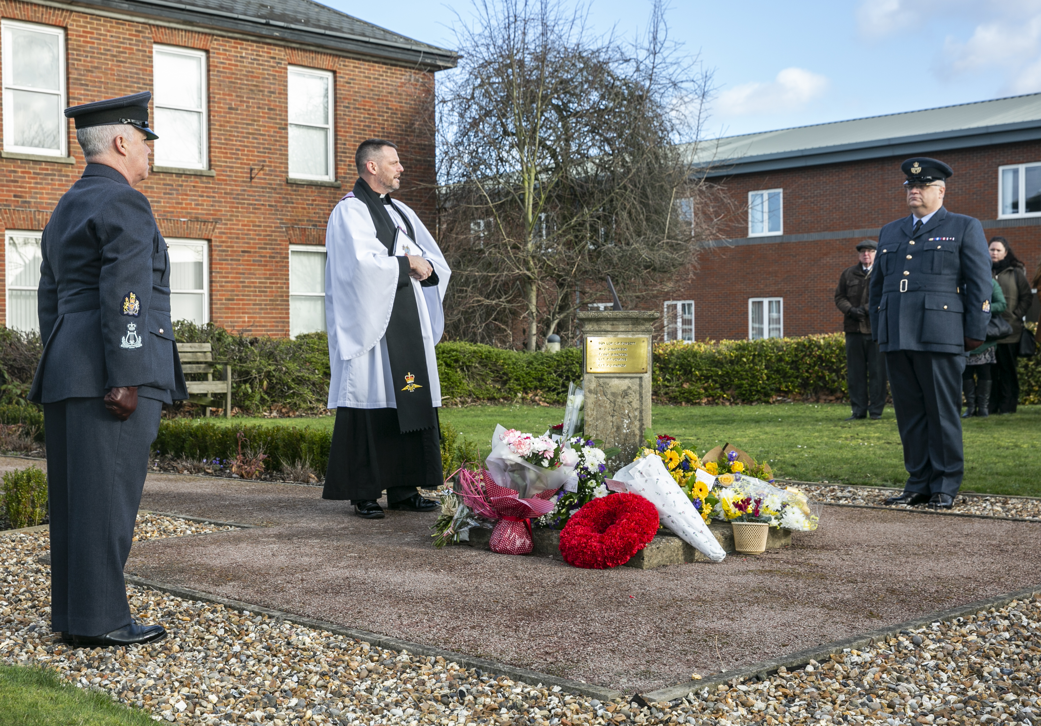 Personnel stand at the memorial and flowers.