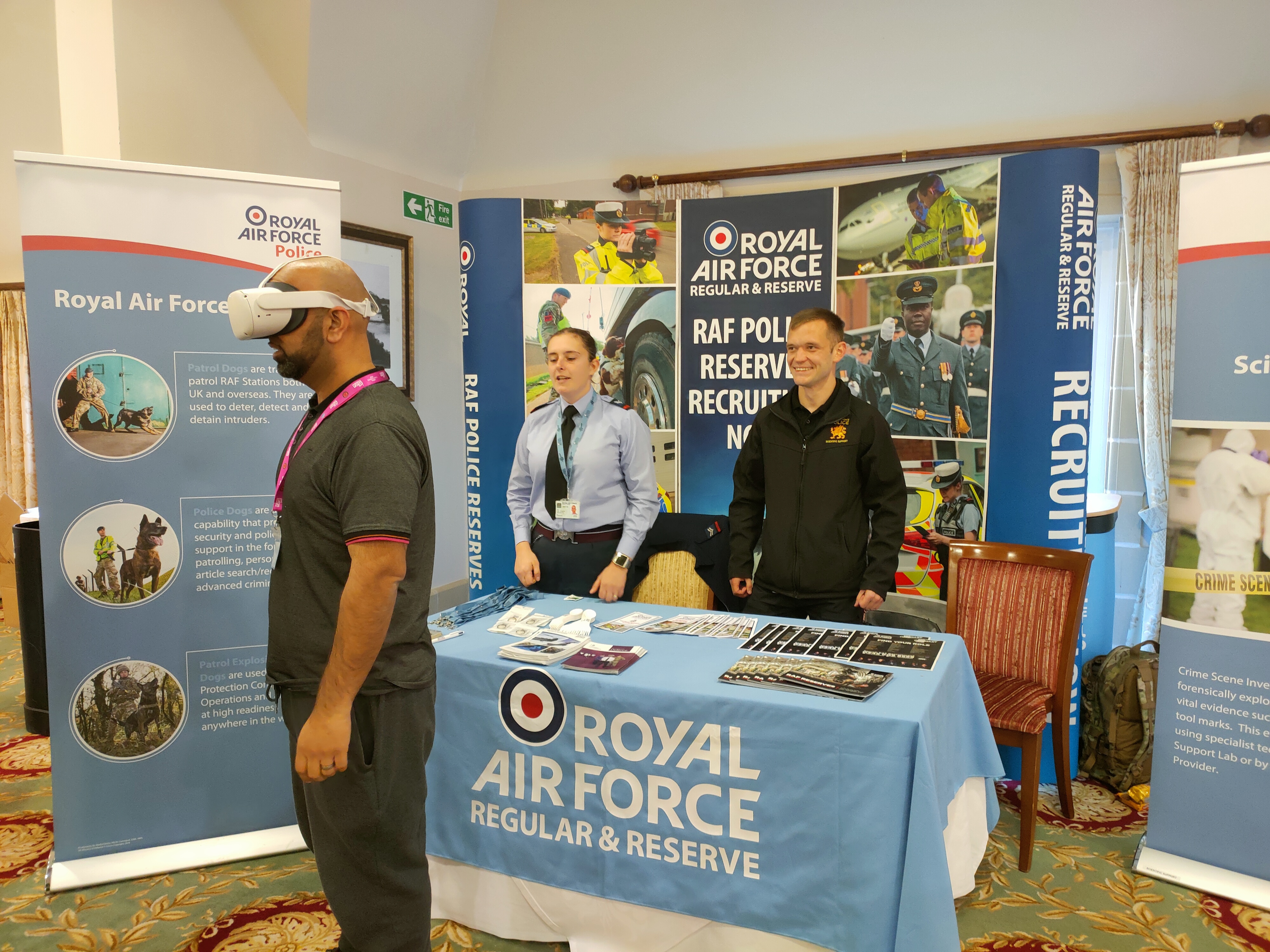 Personnel stand behind table with another using a Virtual Reality Headset.