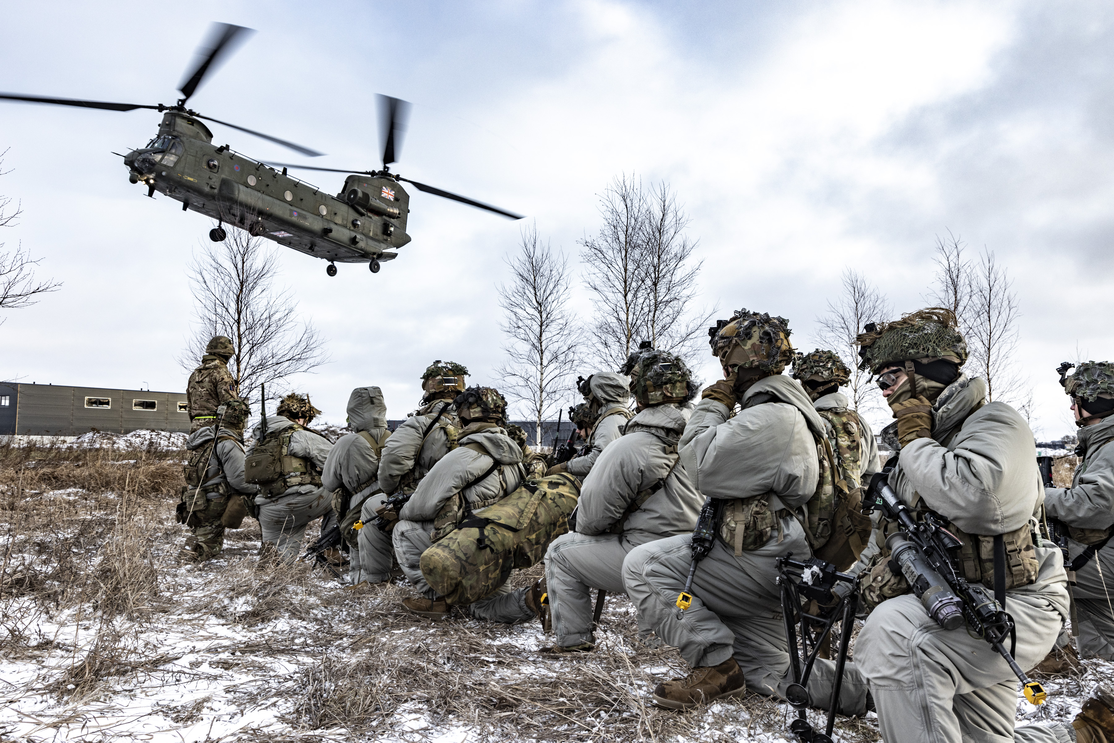 Image shows RAF Regiment kneeling, as a Chinook flies overhead.