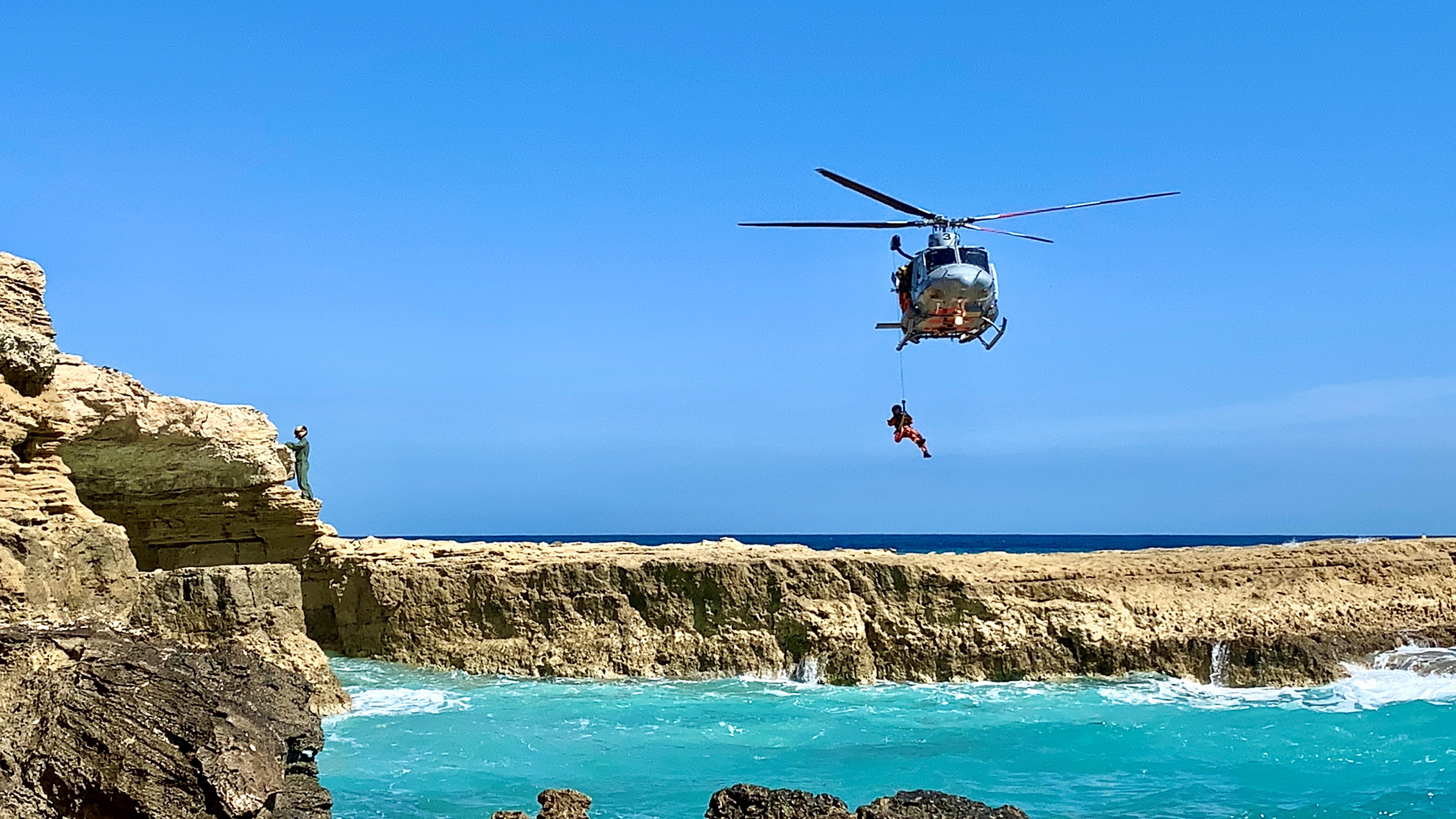 Rescue personnel hang out of helicopter.