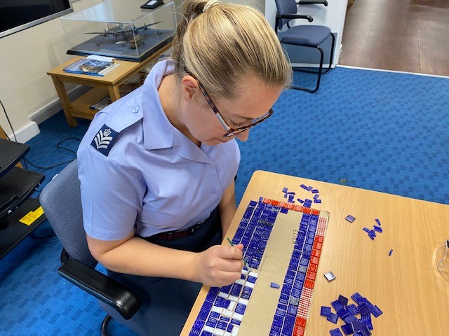 Image shows aviator working on mosaic at a table.
