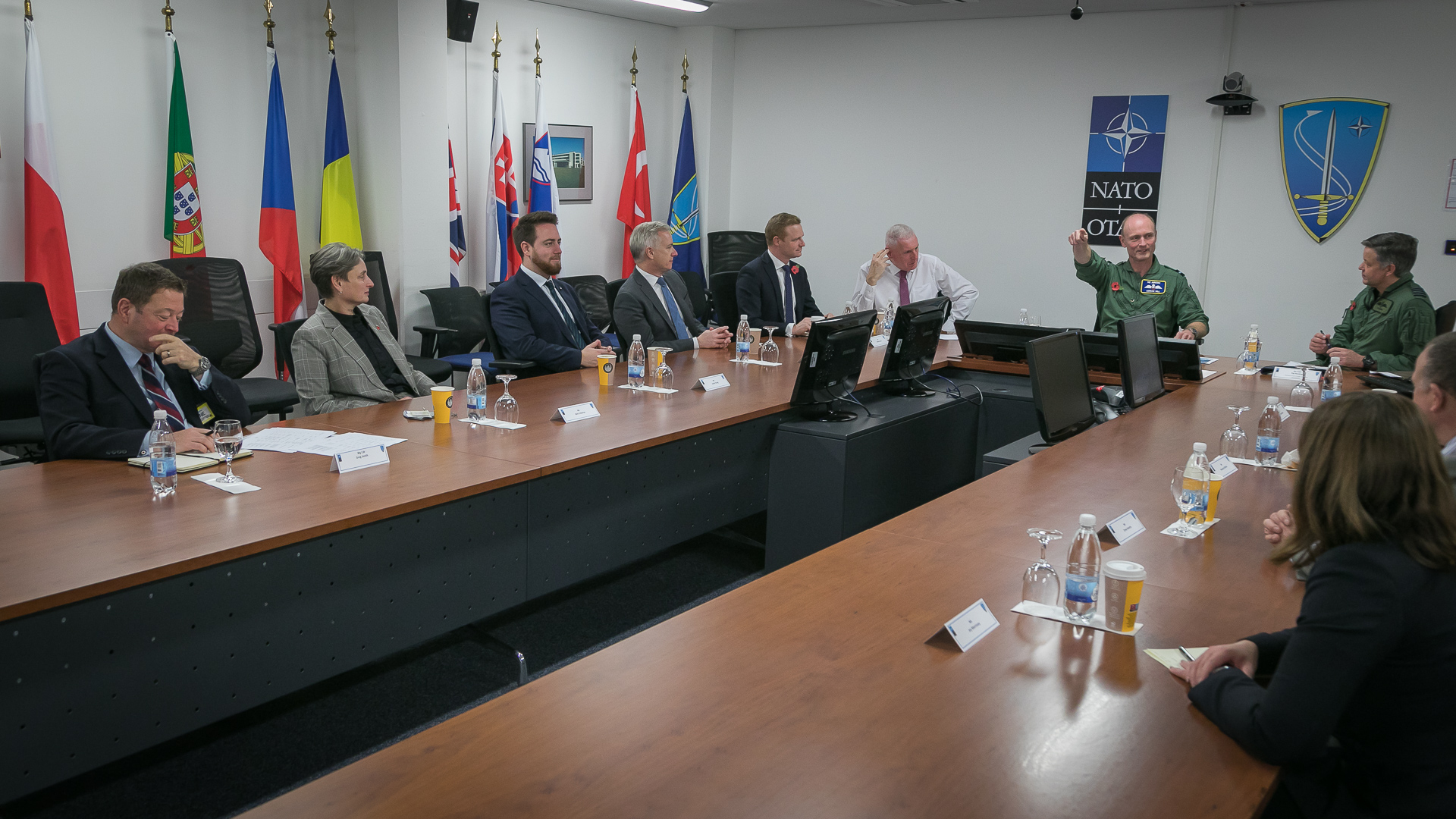 Personnel sit around conference table with flags and computers.