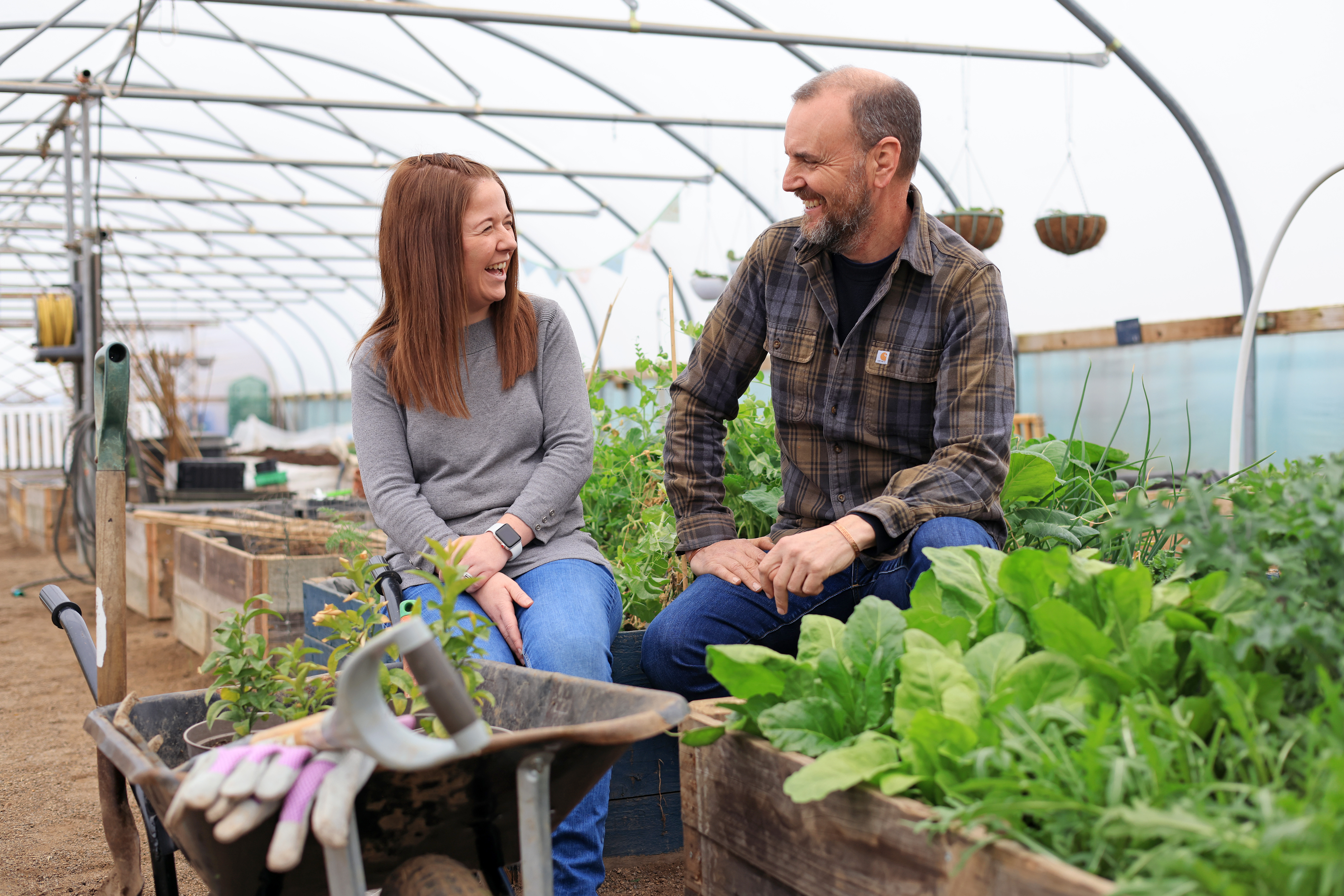 John and Amileigh laugh among plant boxes and gardening equipment.