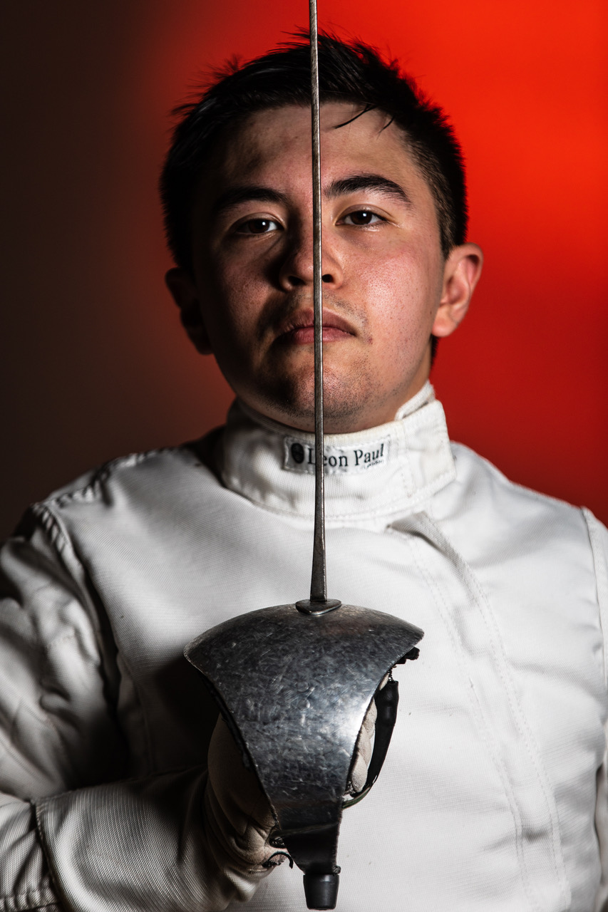 Man holds epee sword to his face.