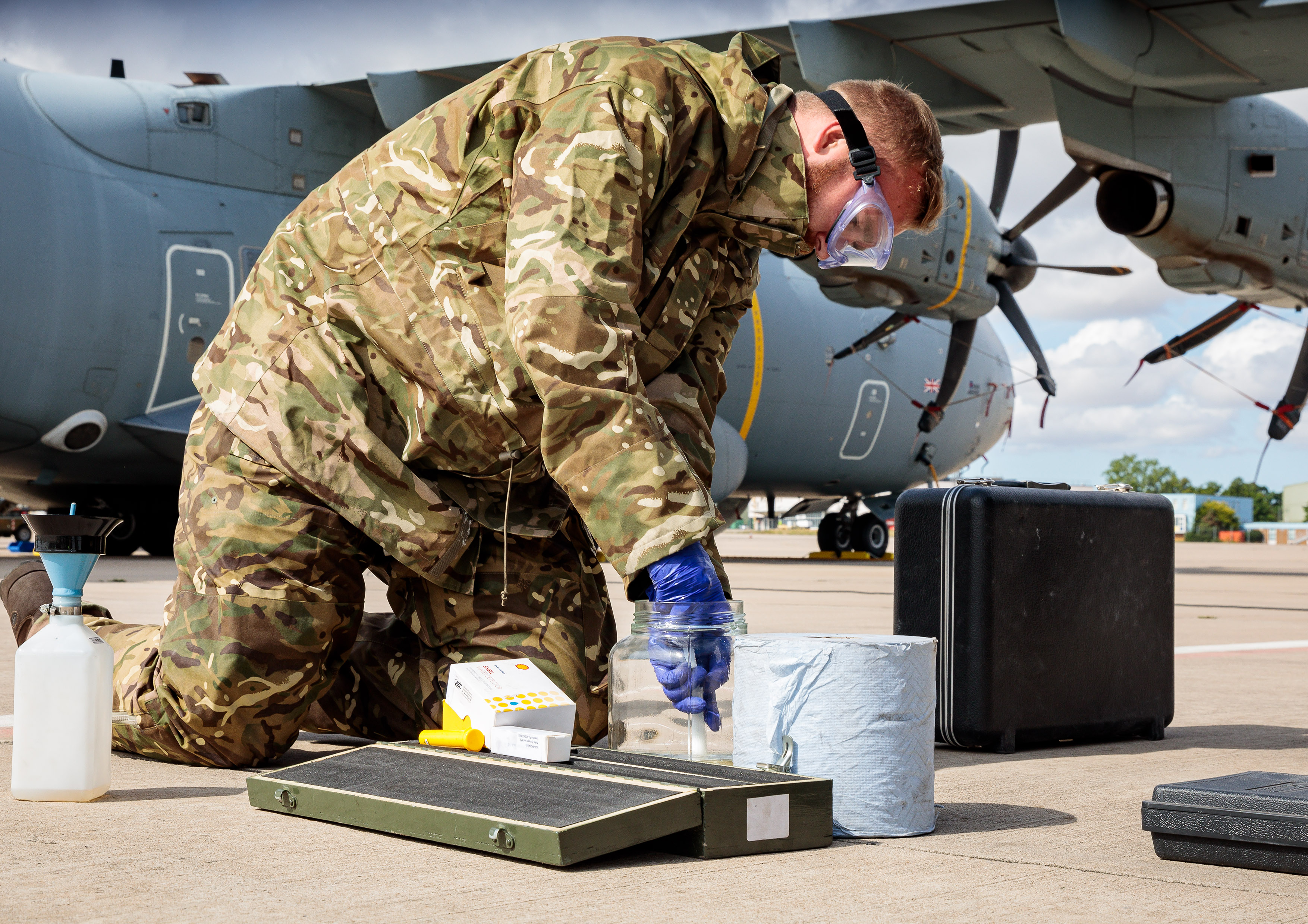 Image shows RAF aviator handling equipment with Hercules aircraft in background. 