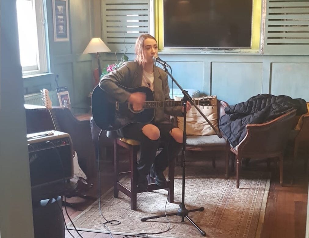 Beth plays a guitar behind a microphone, in a pub.