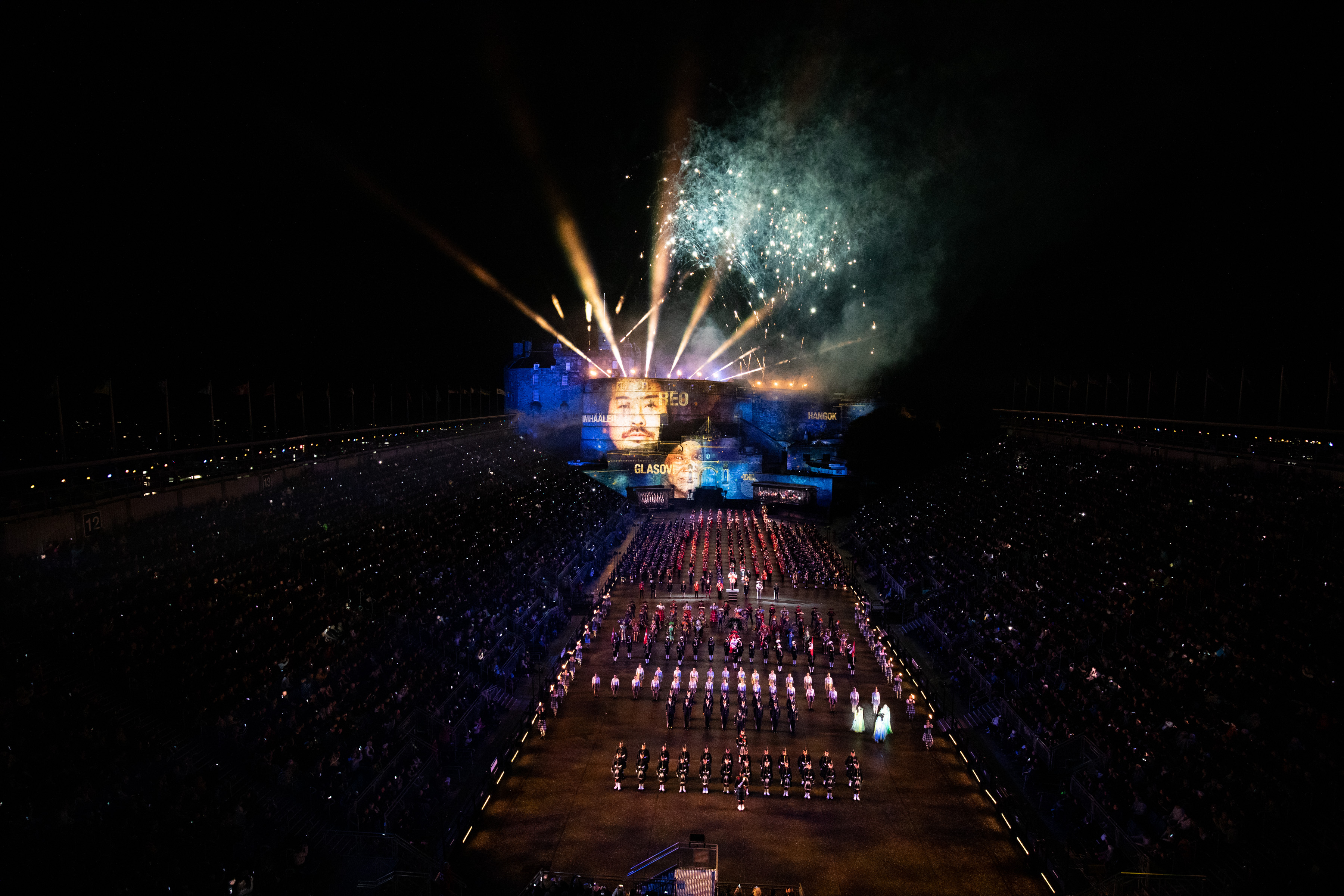 Image shows parade with fireworks and a face projected onto Edinburgh Castle at night.