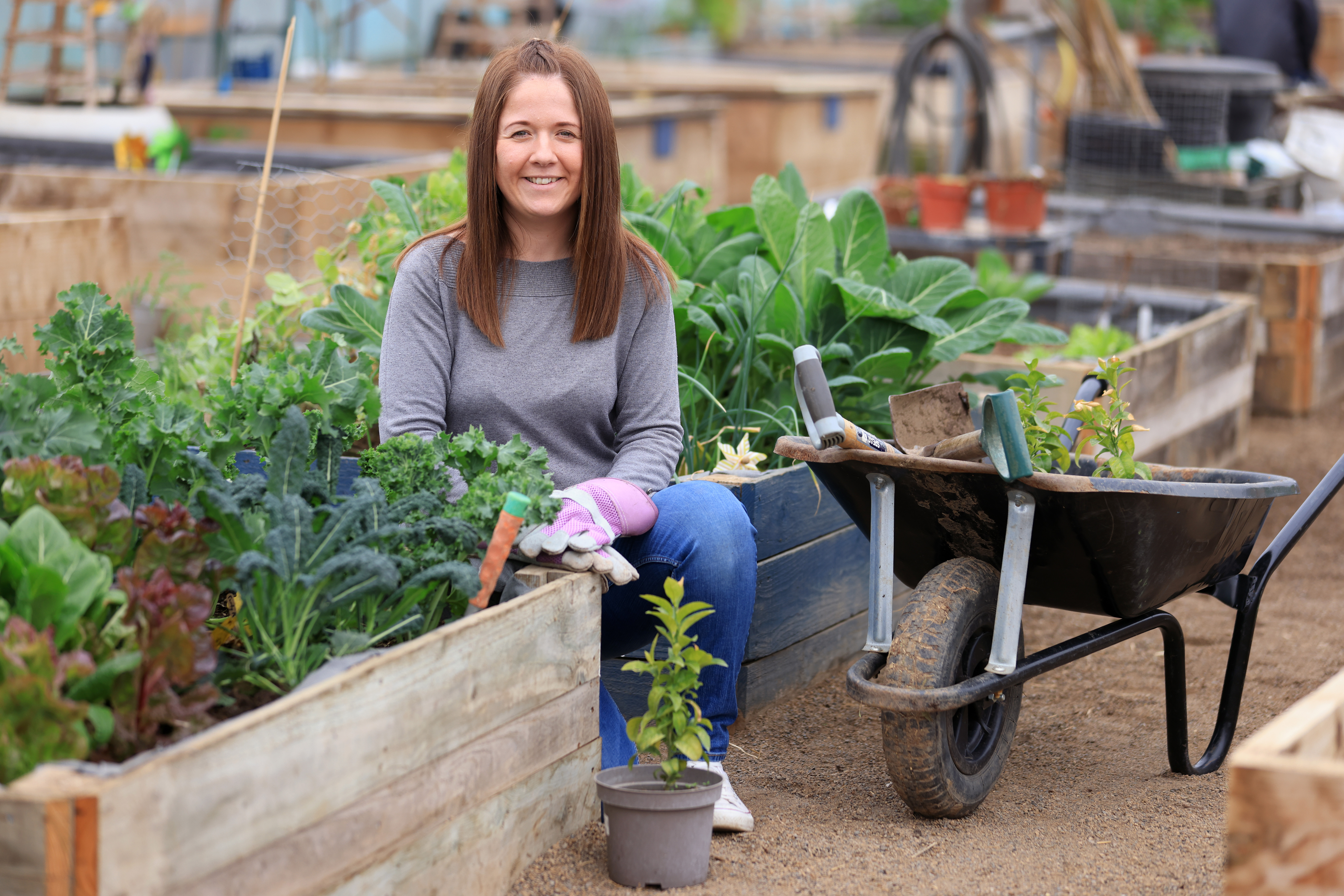 Amileigh sits among plant boxes and wheelbarrow.