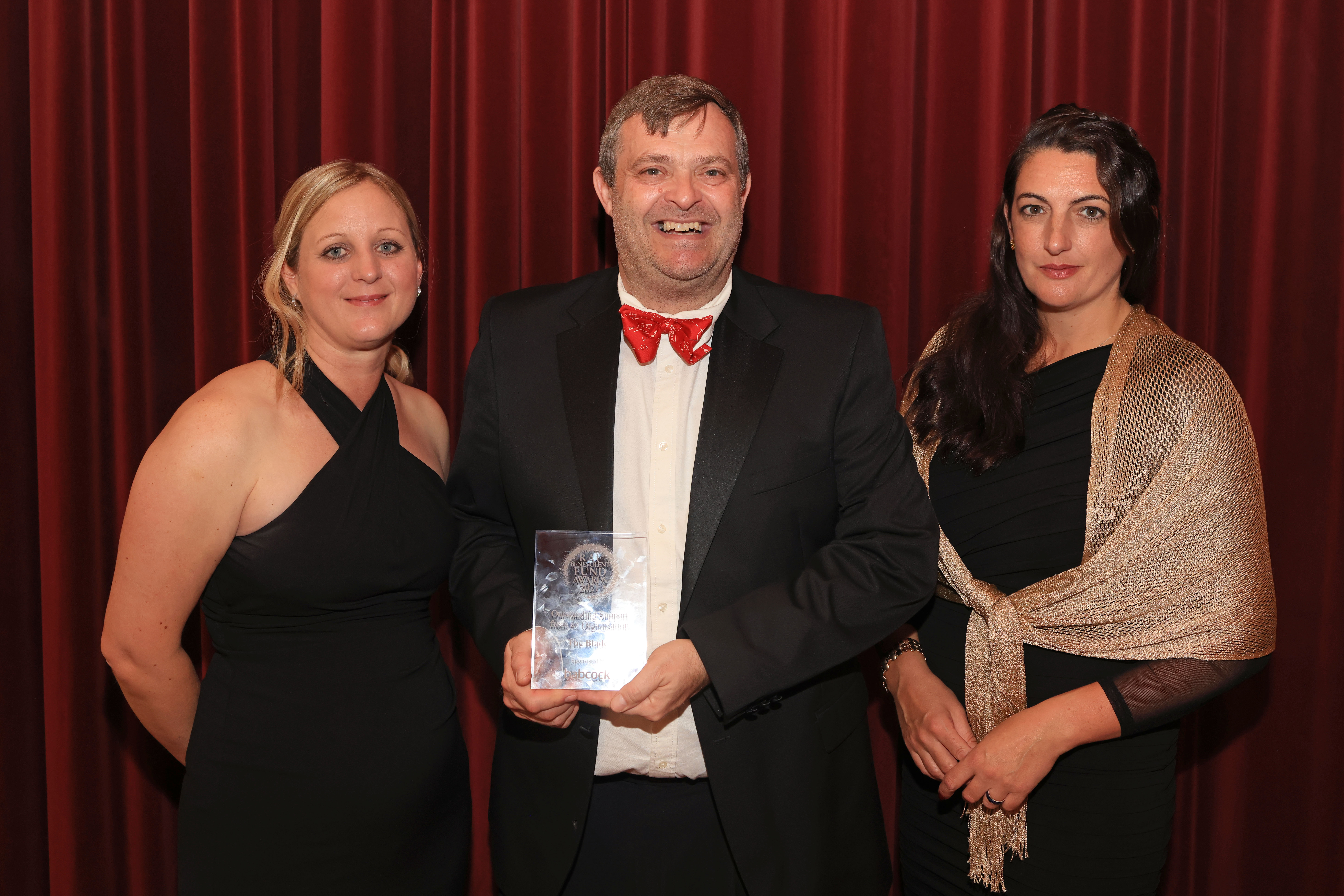 Two women and a man in smart attire hold their award.