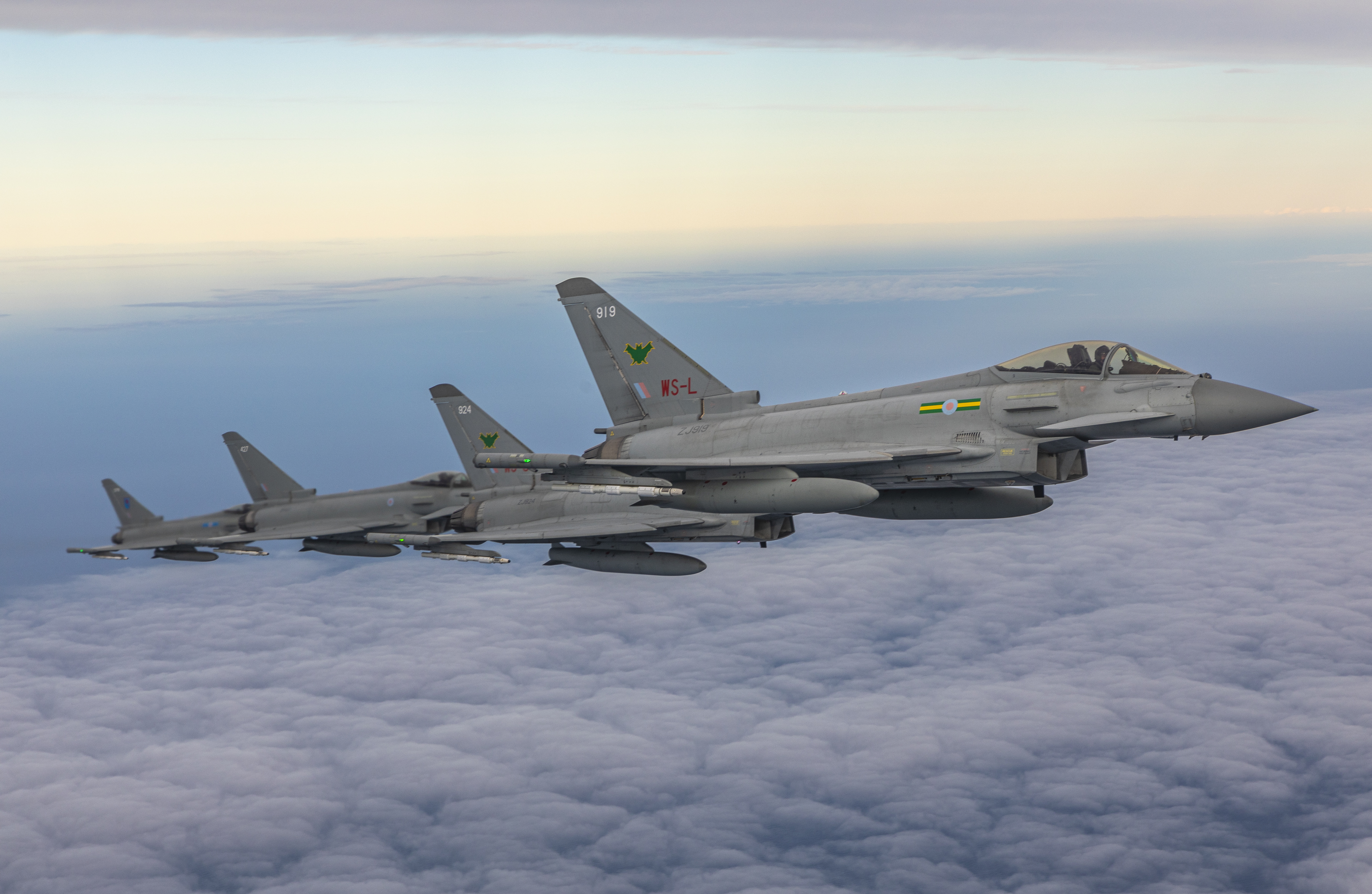 Aircraft fly in formation above clouds.