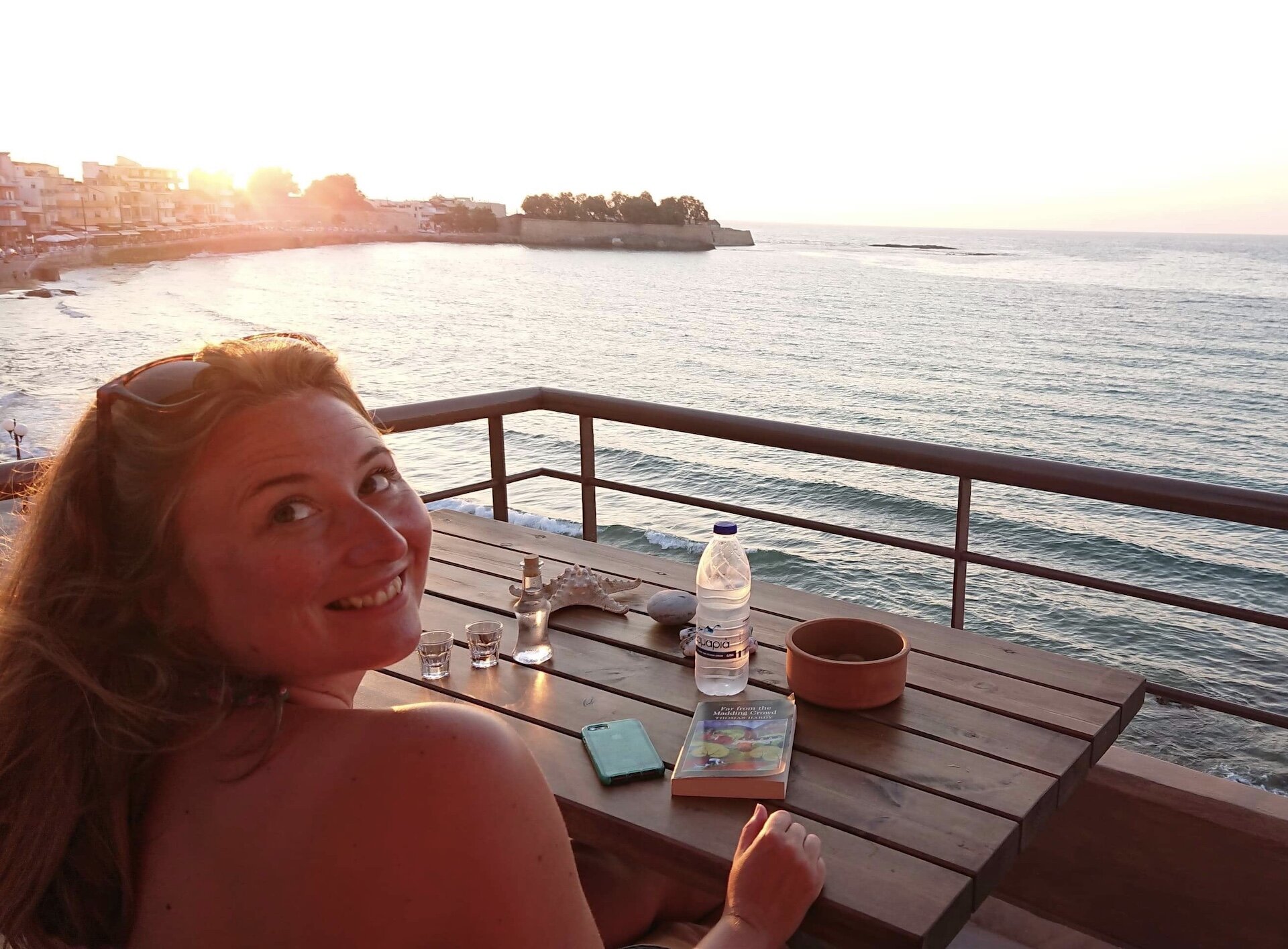 Sophie looks back while sitting at a table overlooking the sea.
