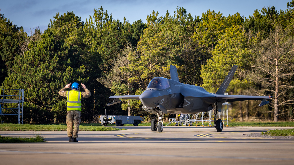 Image shows an RAF aviator guiding a RAF Typhoon on an airfield.