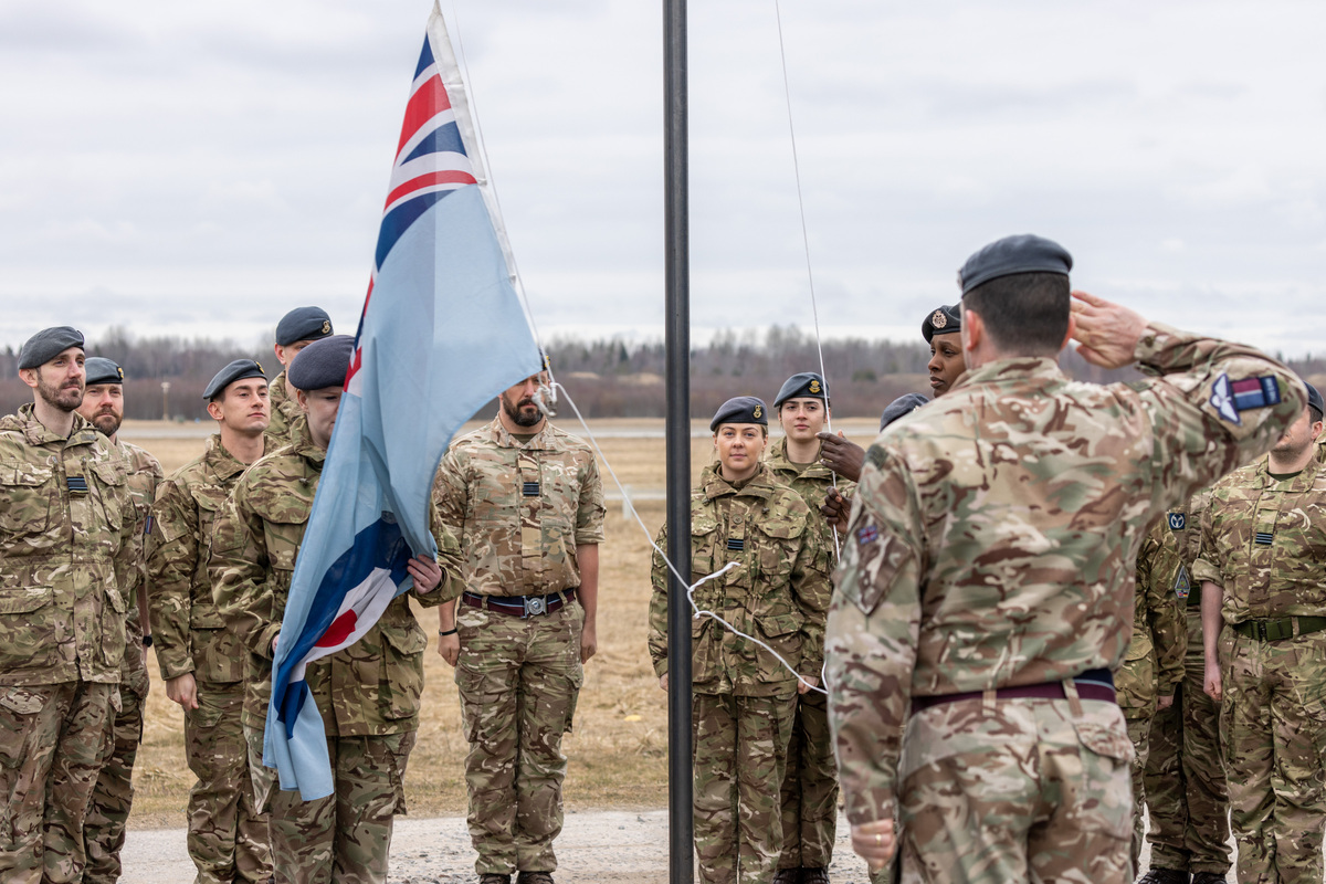 Image shows RAF personnel saluting and standing around flag pole.