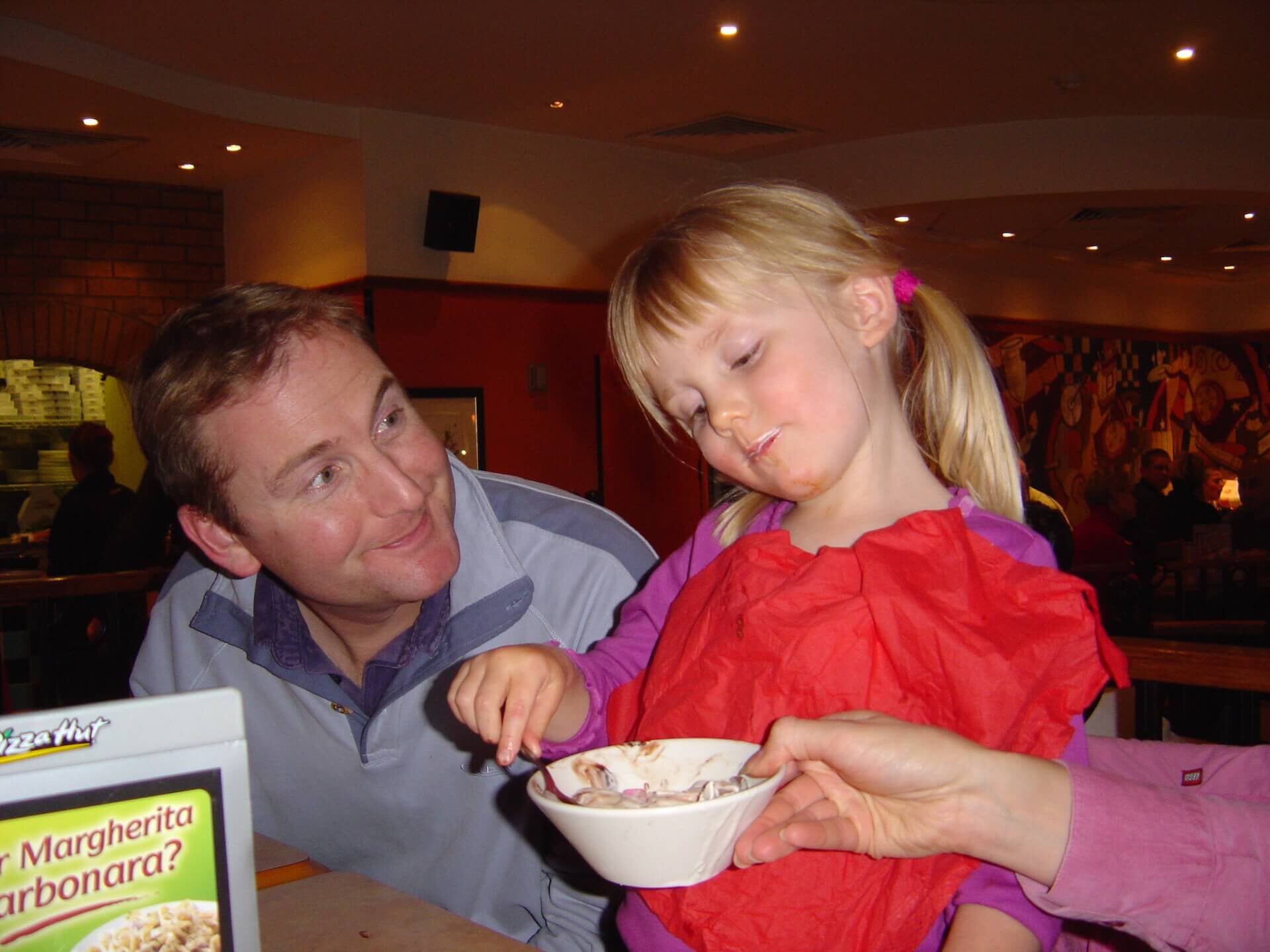 Young Emily eats from a bowl with her father.
