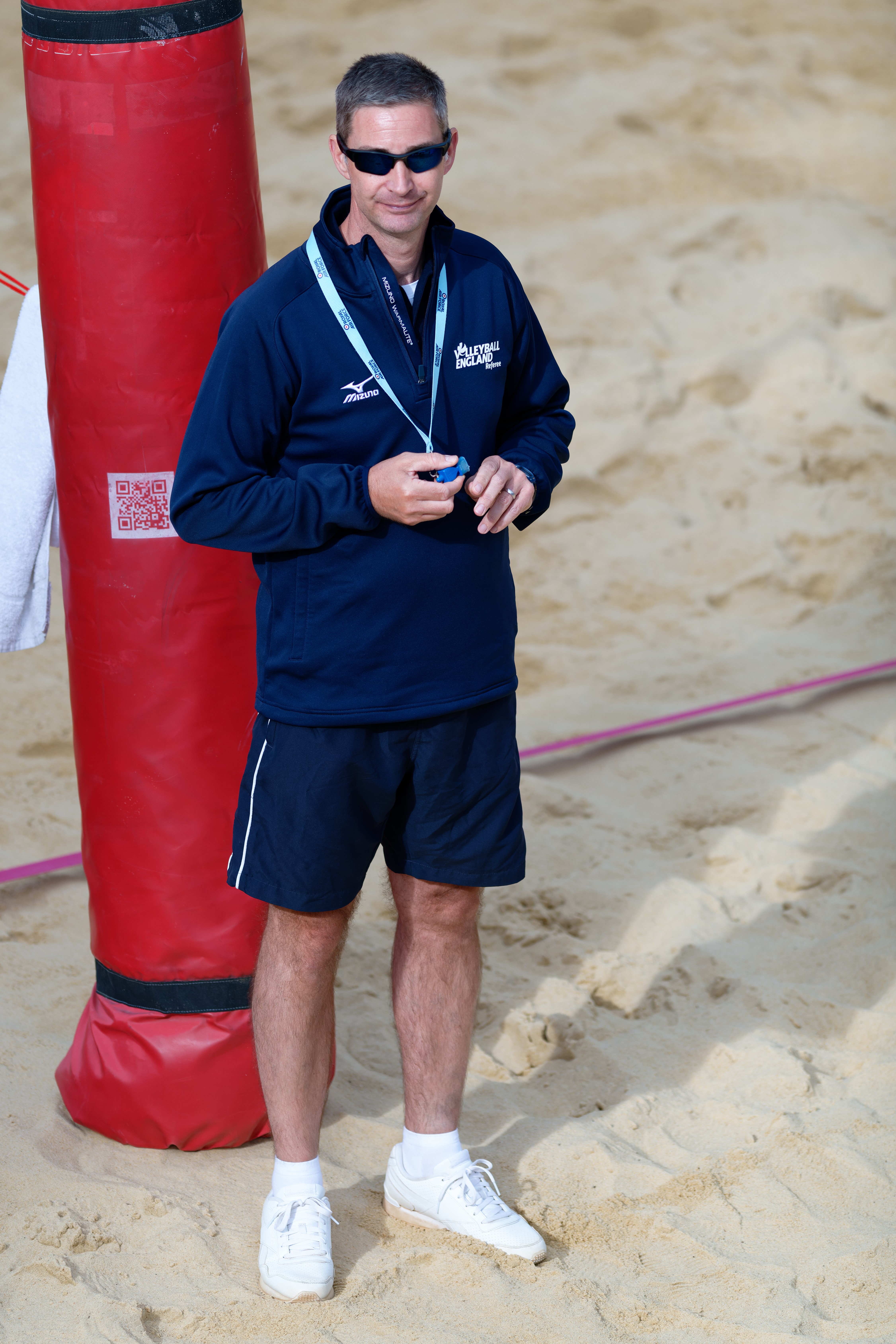 Image shows referee holding whistle on the beach.