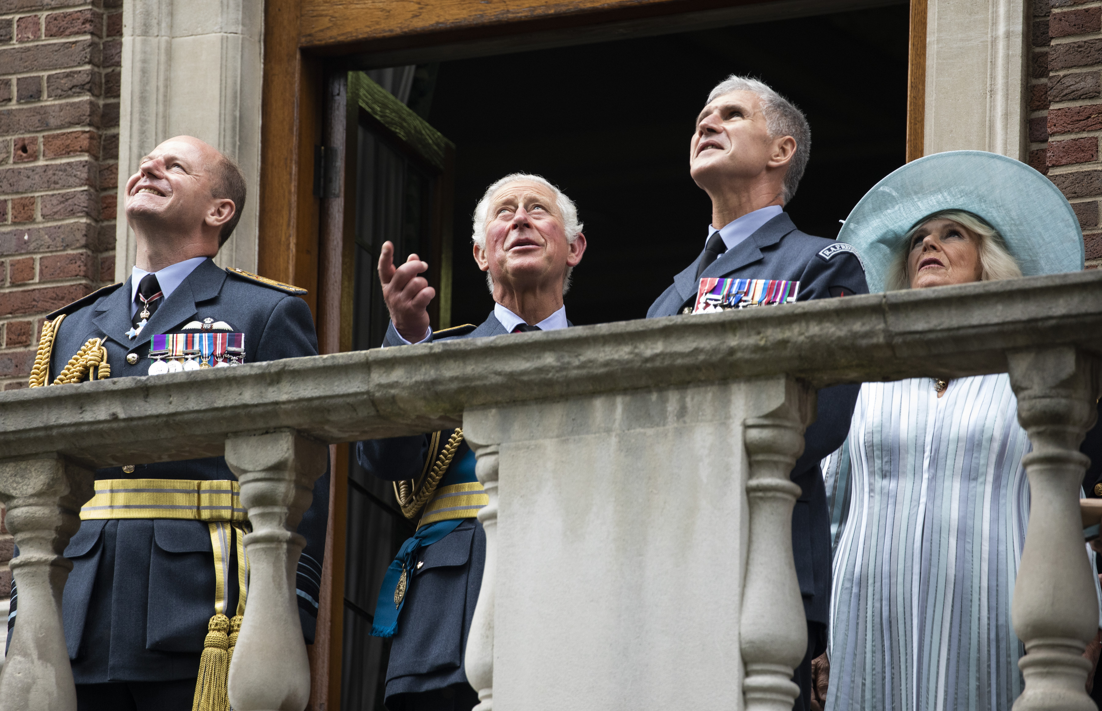 Their Royal Highnesses and Chief of the Air Staff stand on balcony looking up to flypast.