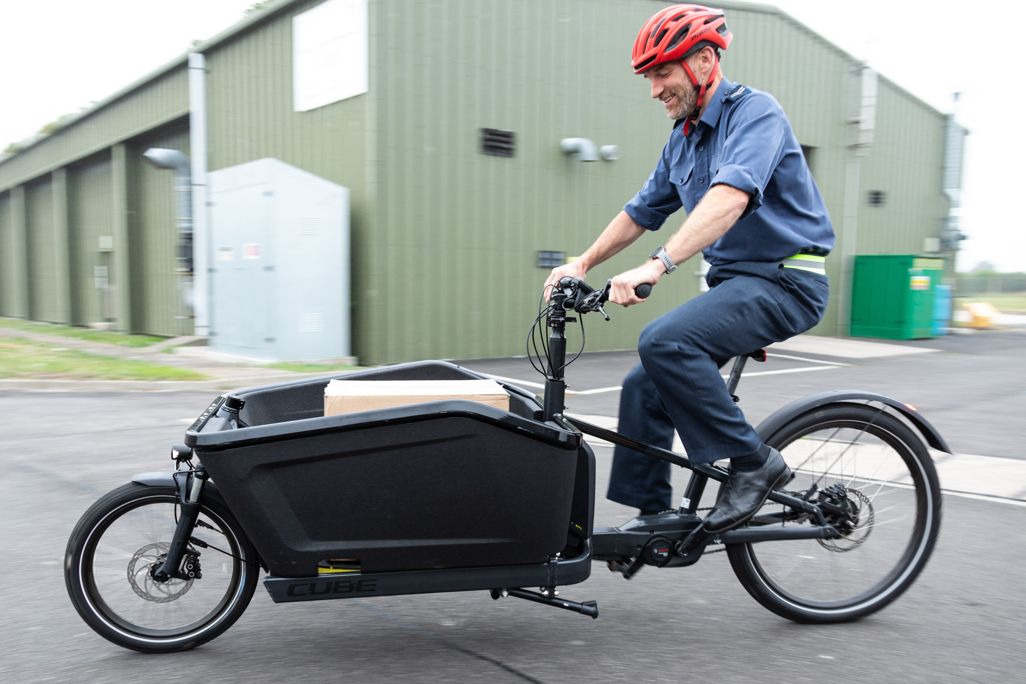 Image shows aviator riding an electric bicycle,.which is carrying cargo at the front. 