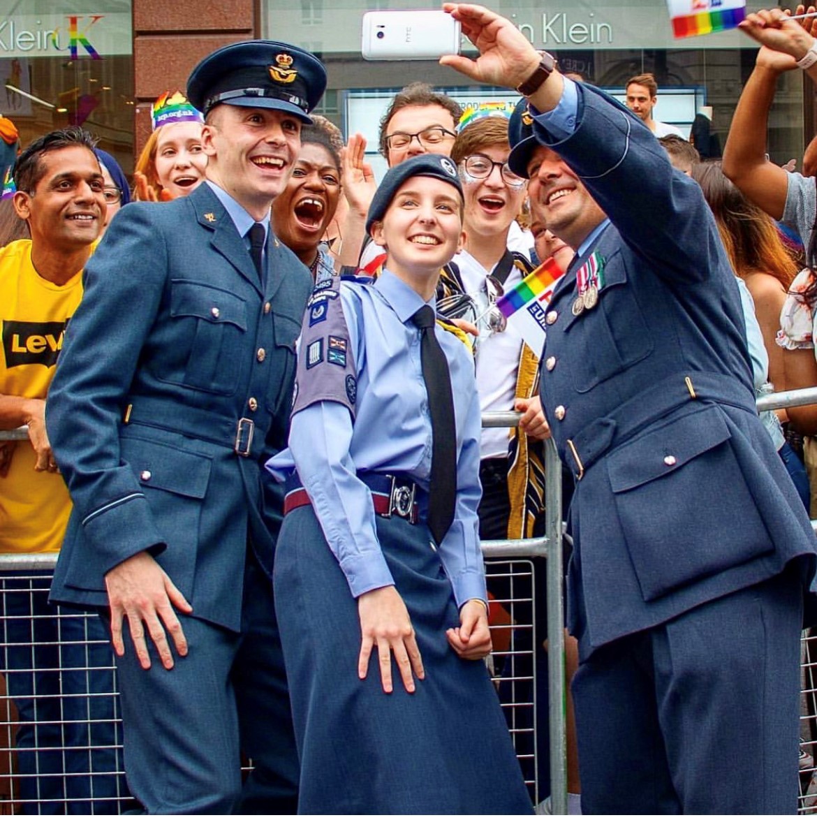 Three personnel smile as they take a selfie during a Pride March.